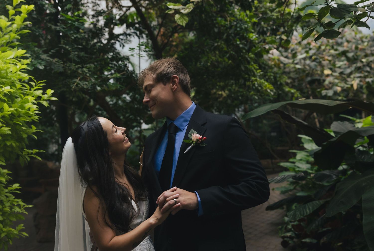Bride and groom share a romantic moment surrounded by lush greenery in an elegant garden wedding setting.