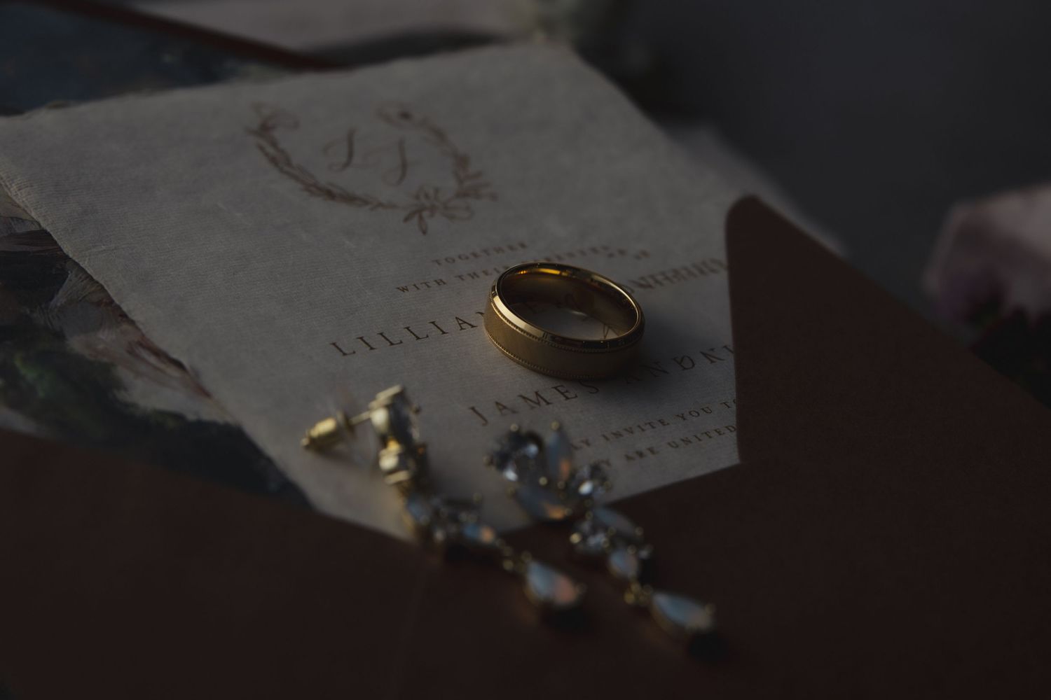 A gold wedding ring sits on a piece of paper alongside scattered small crystals and stones in dim lighting.