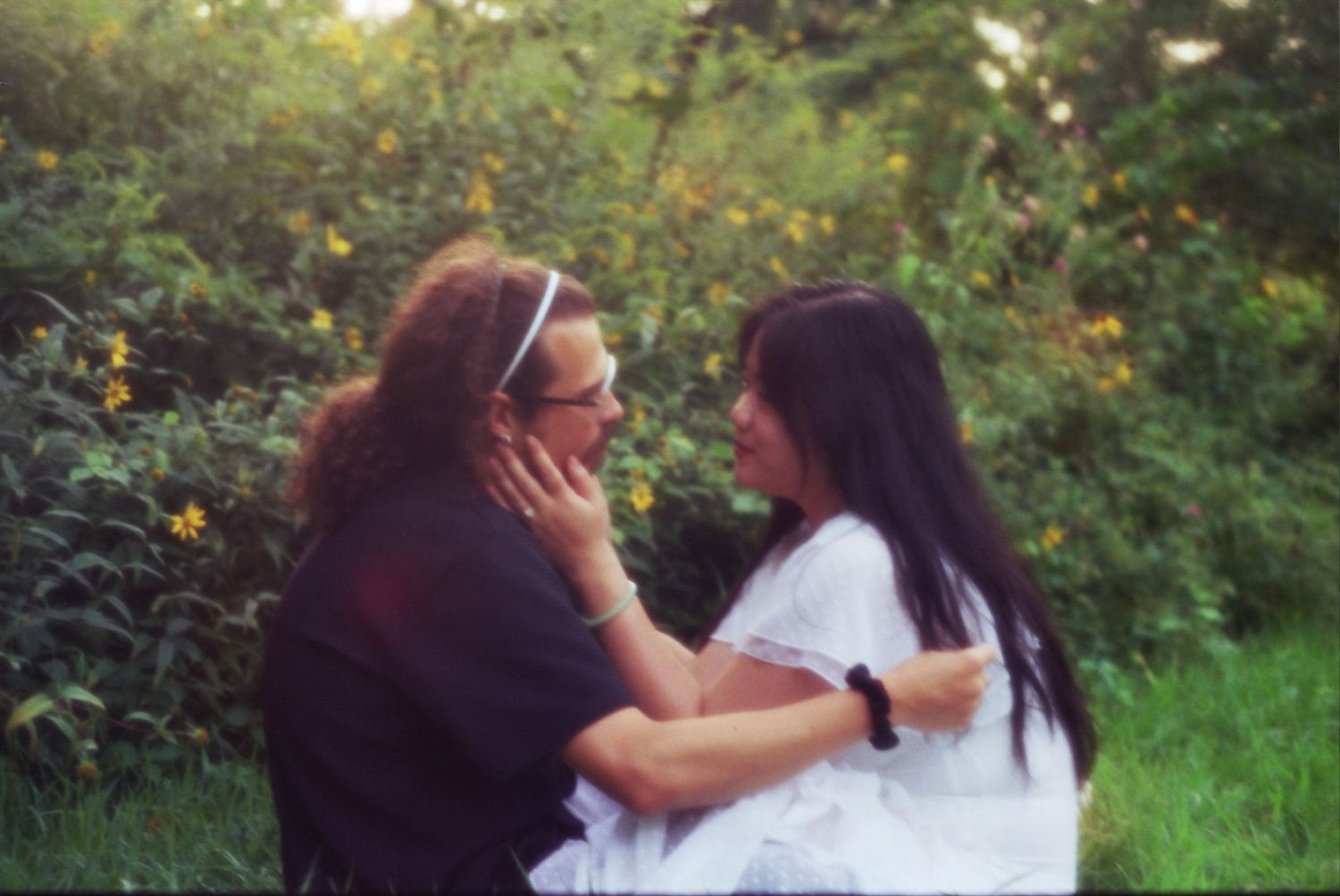 A couple sits close together outdoors surrounded by lush greenery during a romantic photography session.