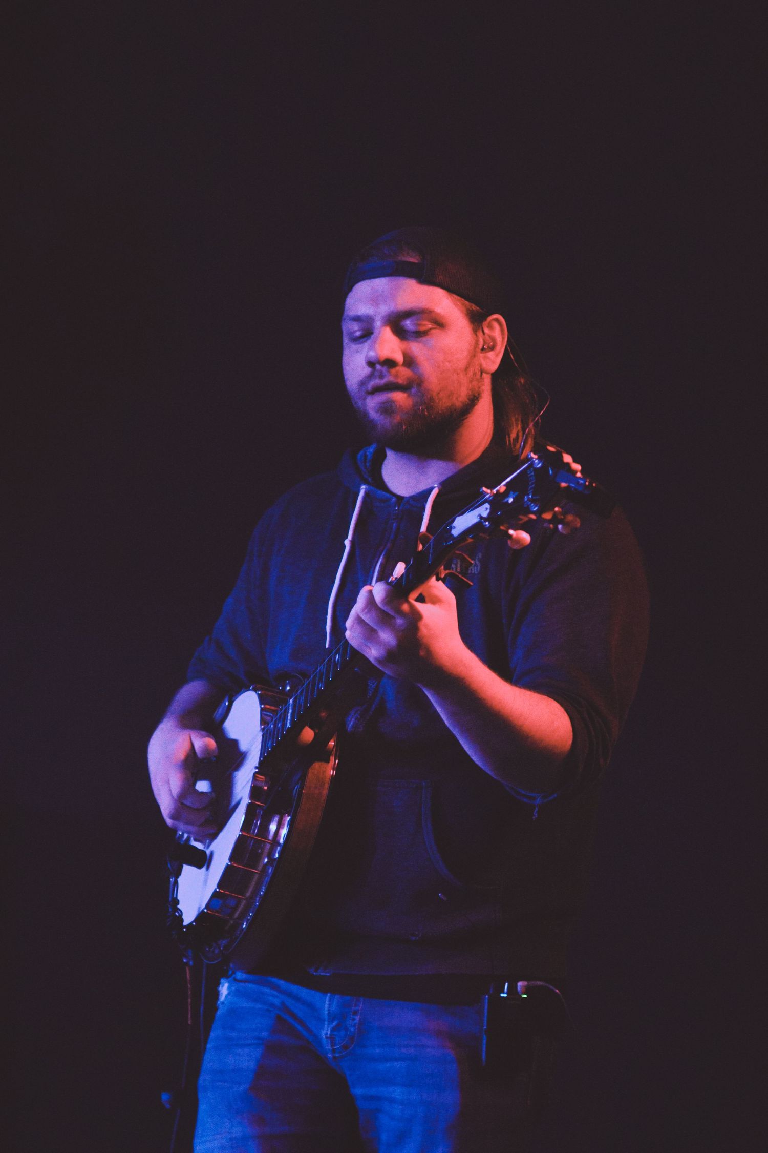 Musicians perform on stage in moody blue lighting with guitar and other instruments.