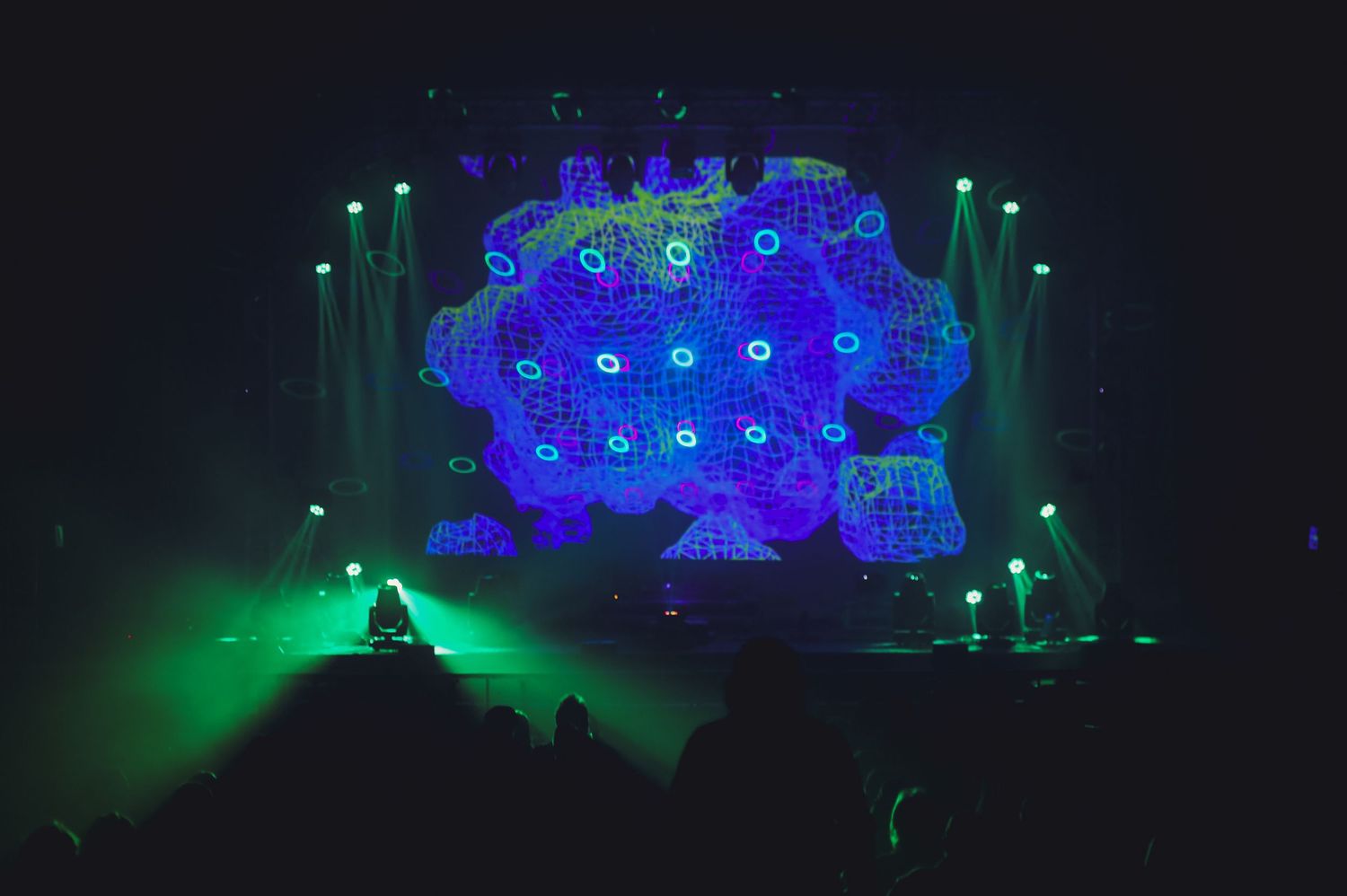 Concert stage illuminated with blue and green lighting effects featuring a large geometric display panel during live performance.
