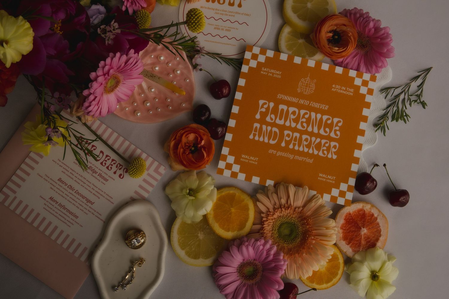 A flatlay composition with colorful gerbera daisies, citrus slices, and an orange book cover against a soft background.