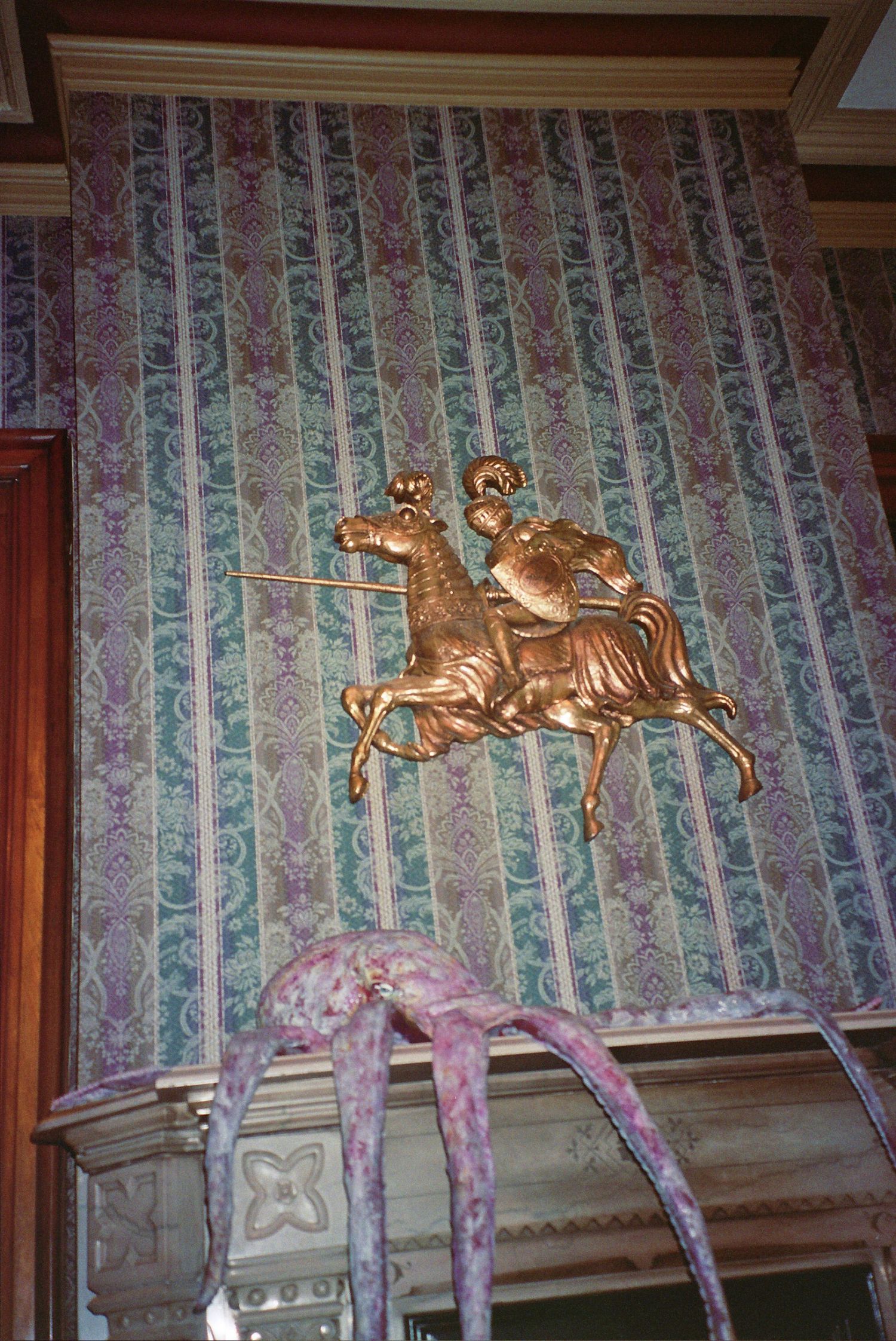 Golden knight on horseback relief sculpture mounted on ornate striped damask wallpaper in elegant interior.