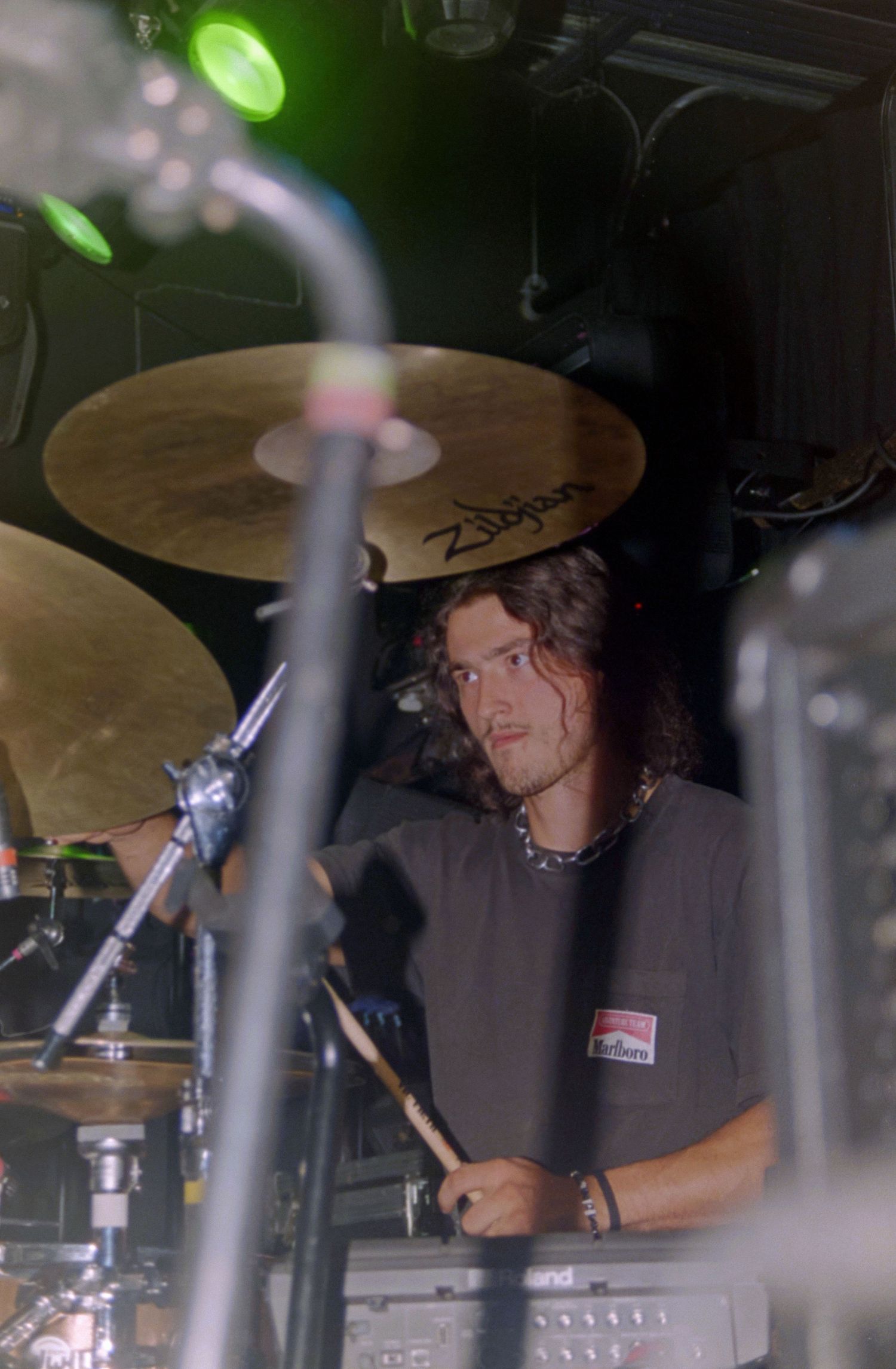 Young male drummer playing Zildjian cymbals on stage in a dark venue, holding drumsticks mid-performance.