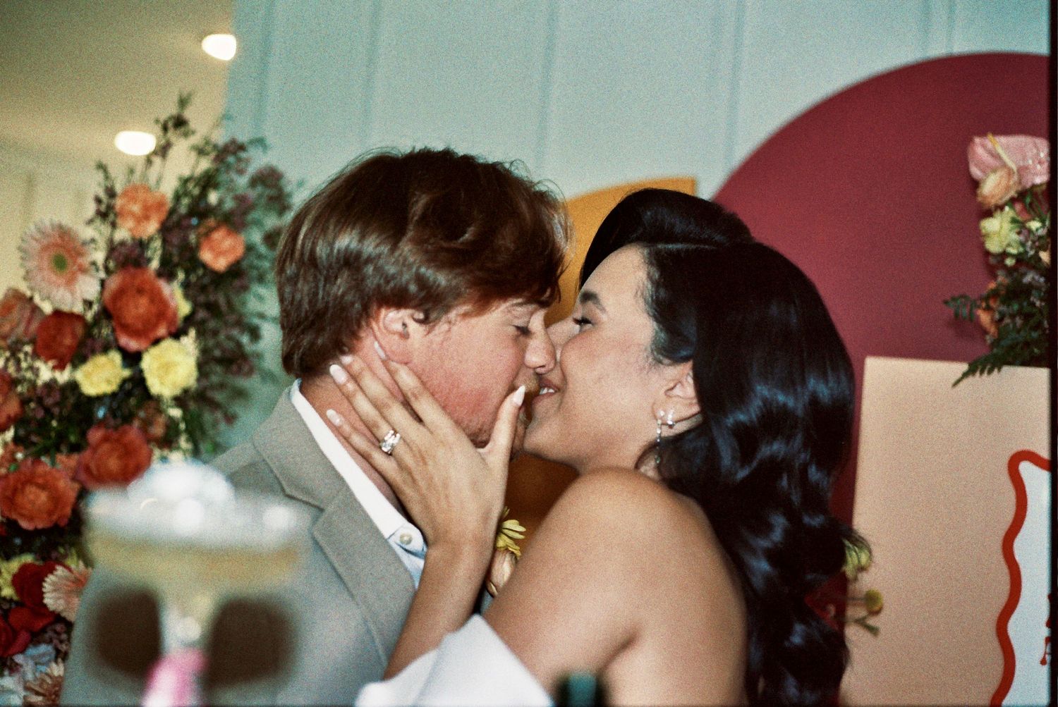 A tender kiss shared between newlyweds at their wedding reception surrounded by pink roses and decorative details.