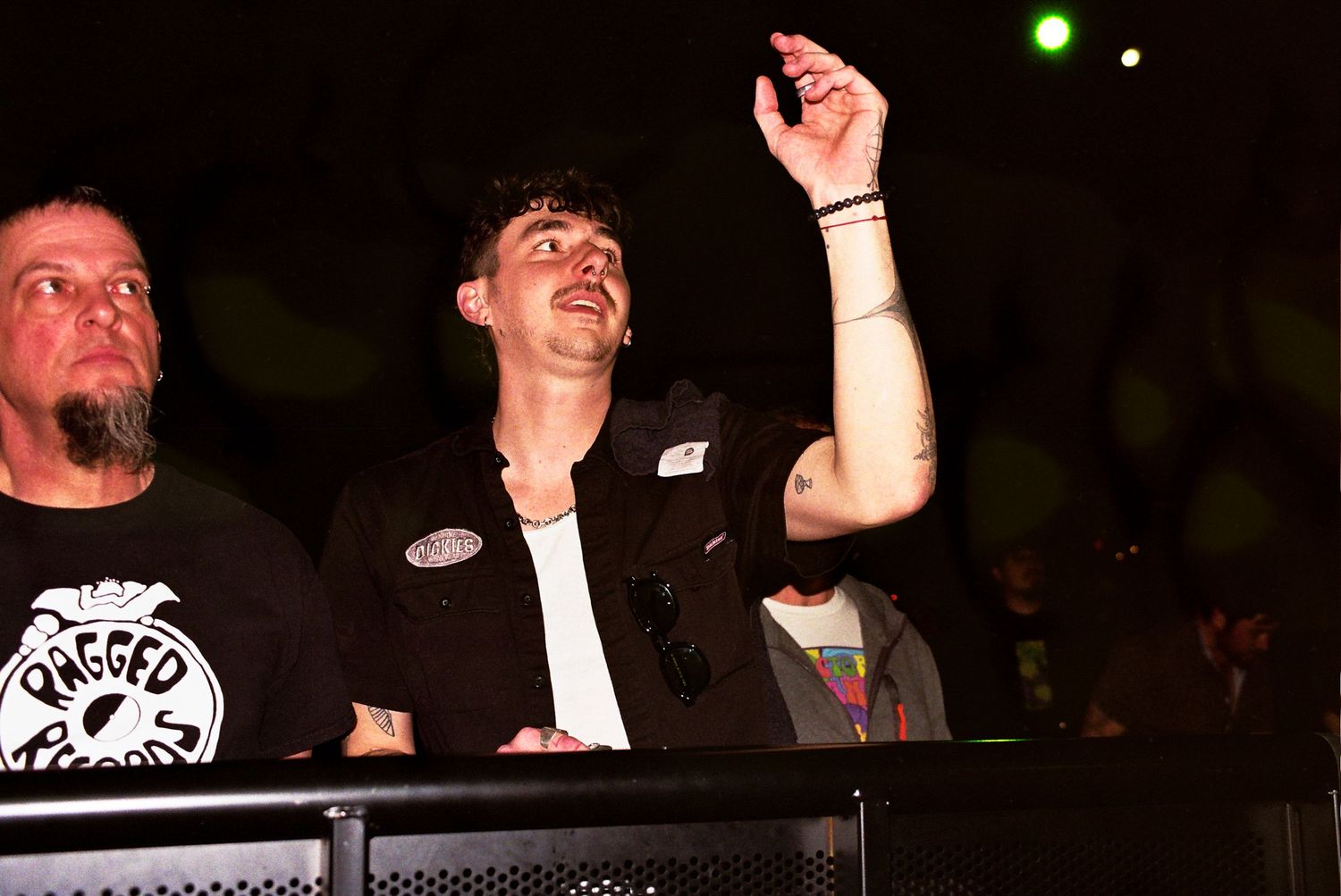 Musicians energetically performing at a concert with stage lighting visible in the dark background.