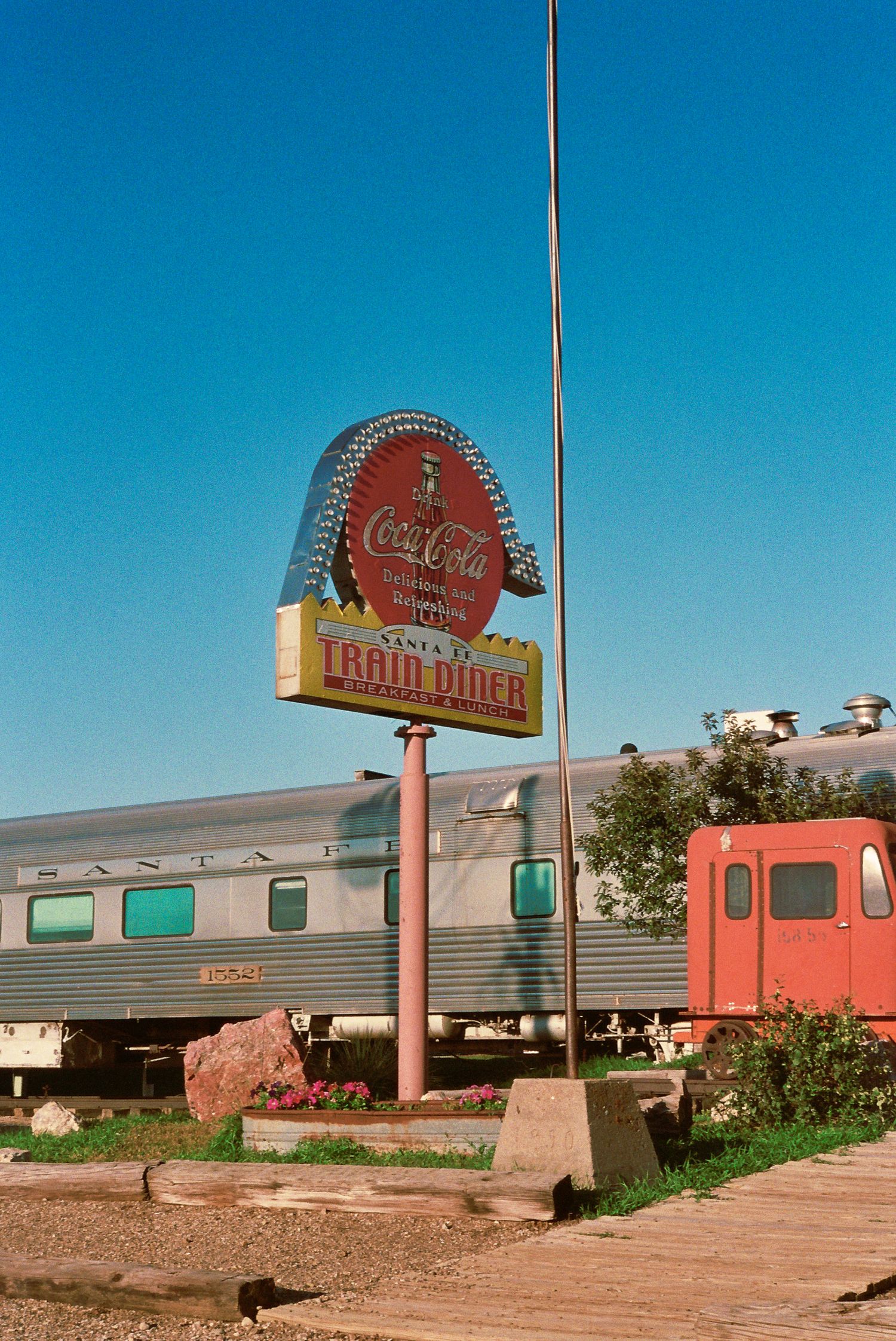 Vintage Coca-Cola diner sign with stainless steel railroad car style building under bright blue sky.