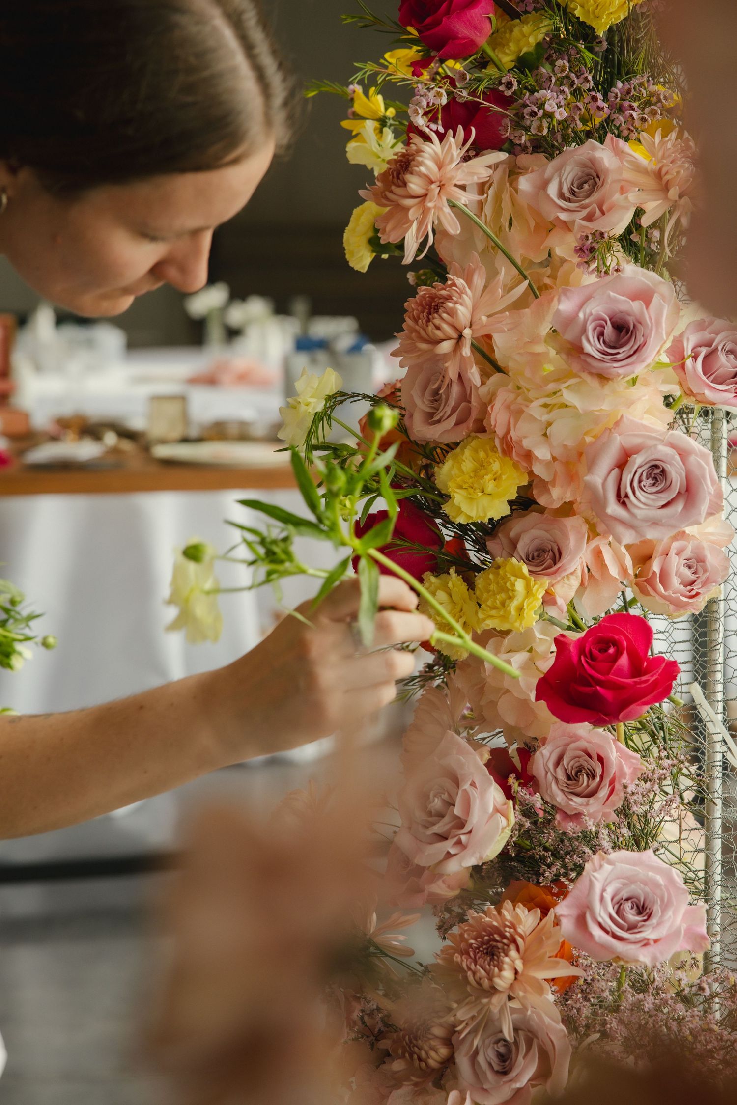 Close-up of hands arranging delicate pink and yellow flowers in an elegant floral centerpiece display.