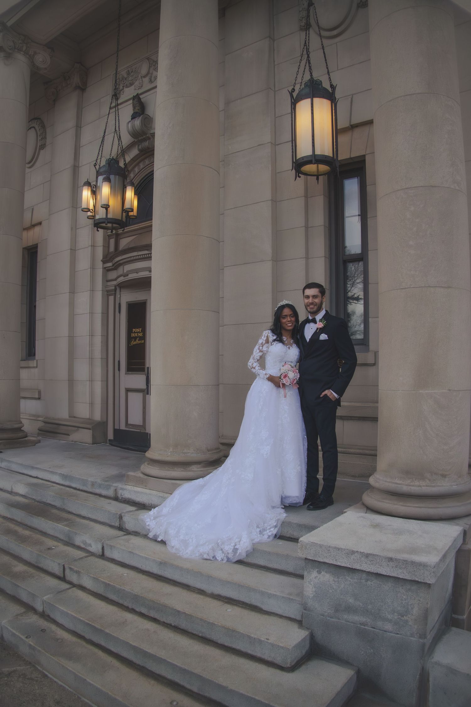 A classic wedding portrait on stone steps of a historic building with hanging lanterns.