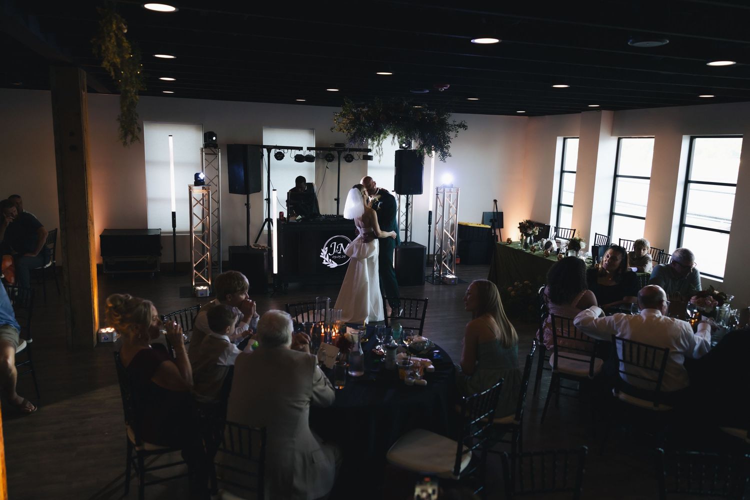 Bride and groom share first dance at elegant wedding reception with guests seated at candlelit tables.
