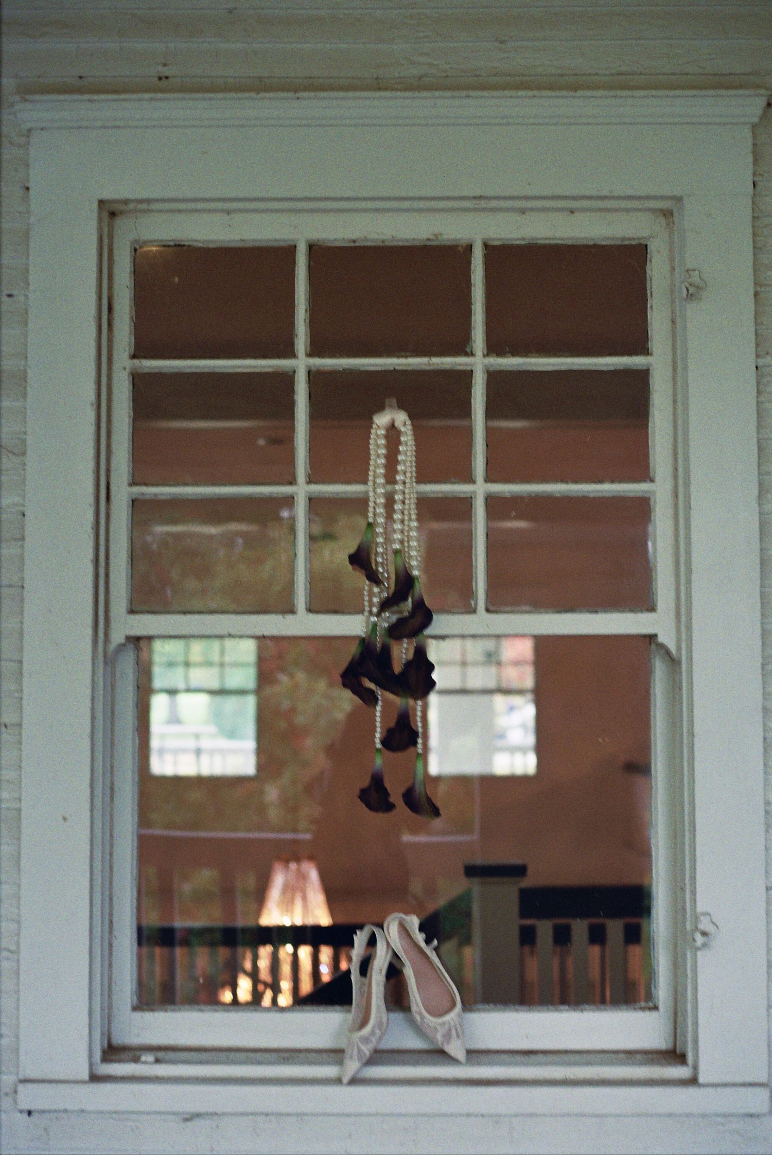 A vintage window displays a hanging doll with beads and ballet shoes resting on the sill, creating an eerie nostalgic scene.