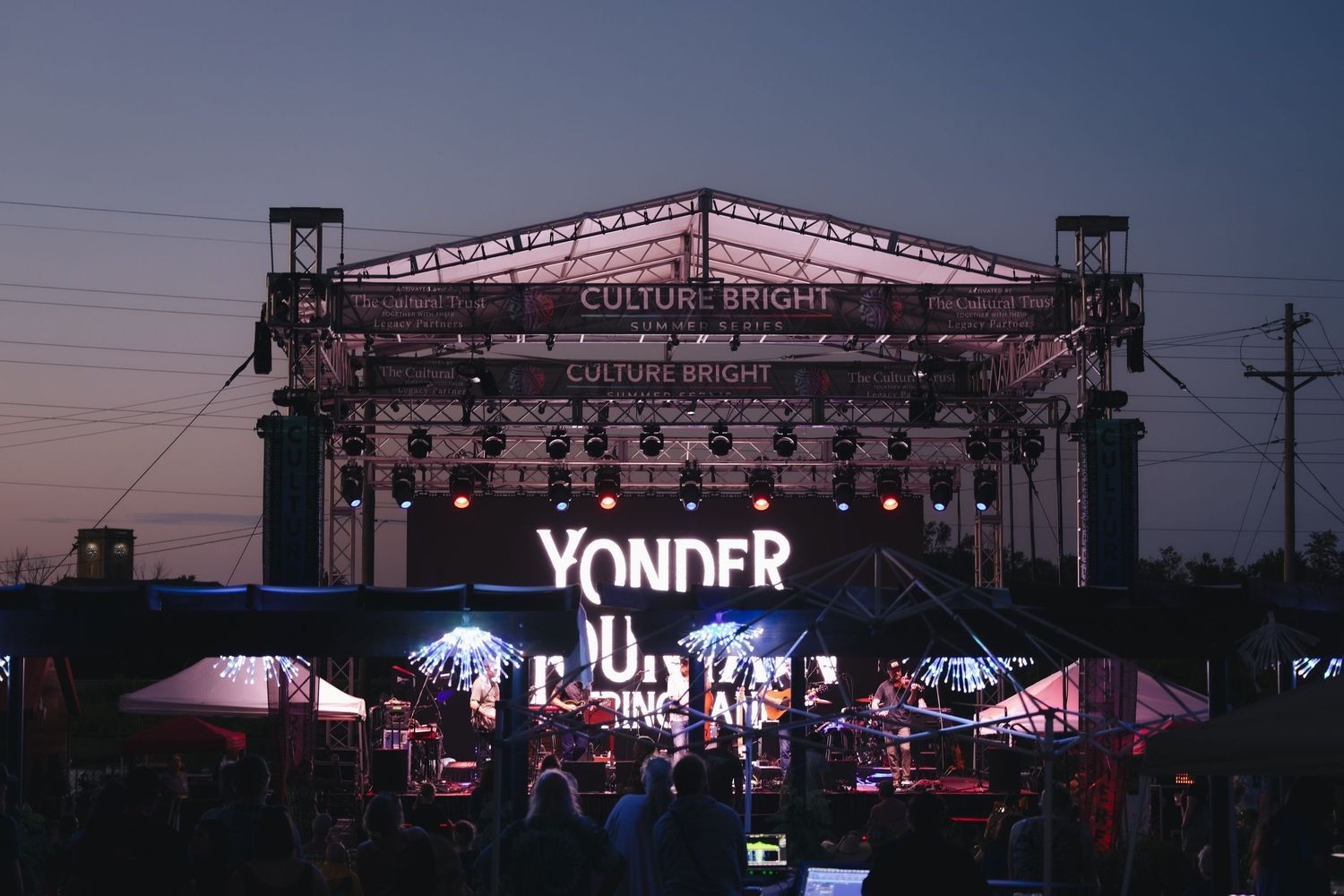 Yonder music festival stage lit up at dusk with colorful lights and crowd gathered below.