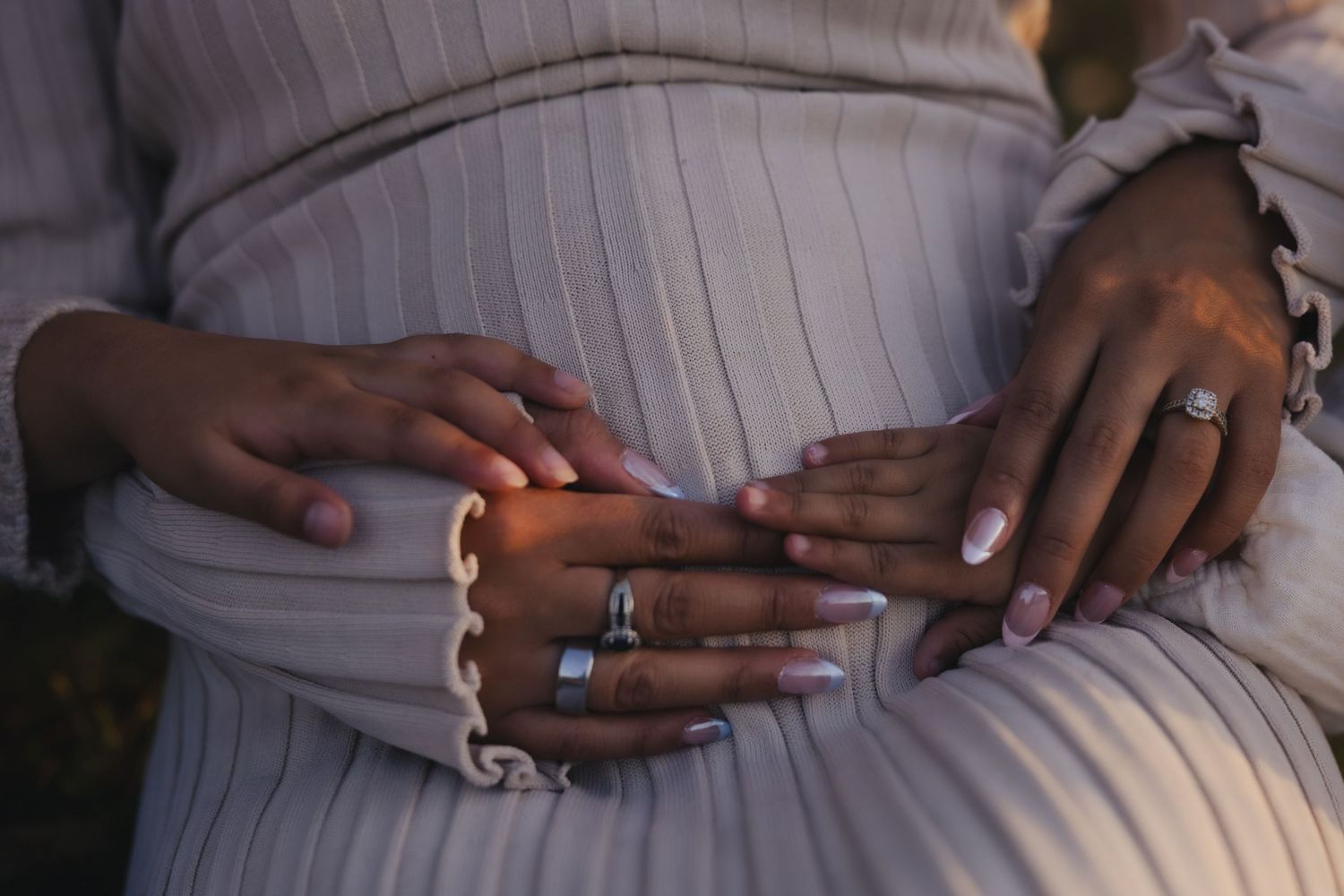 Close-up view of hands with rings resting on white pinstripe fabric.