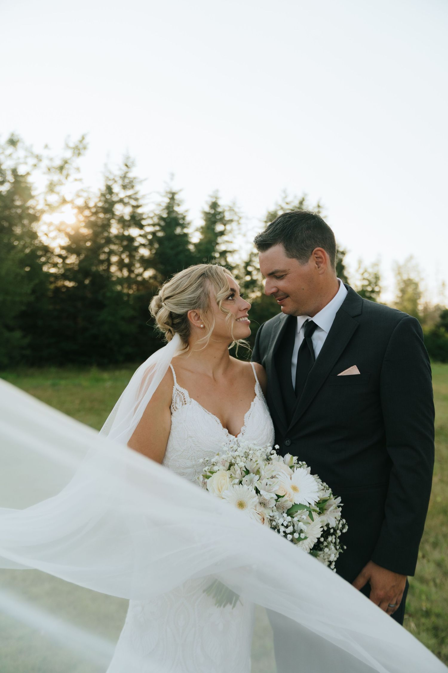 A romantic wedding portrait with flowing veil and white bouquet in golden evening light.