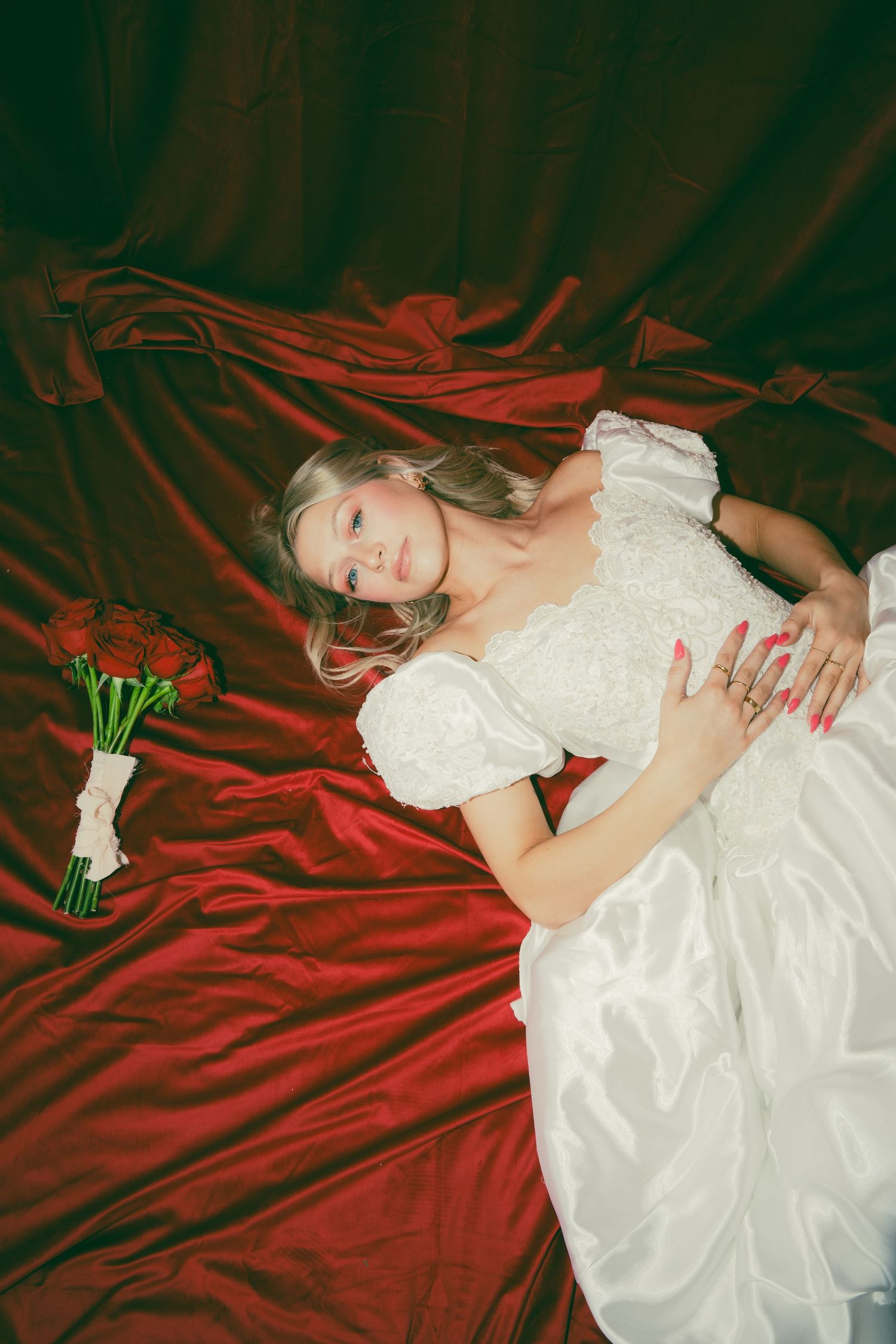 White wedding dress against dramatic red velvet backdrop with floral bouquet.