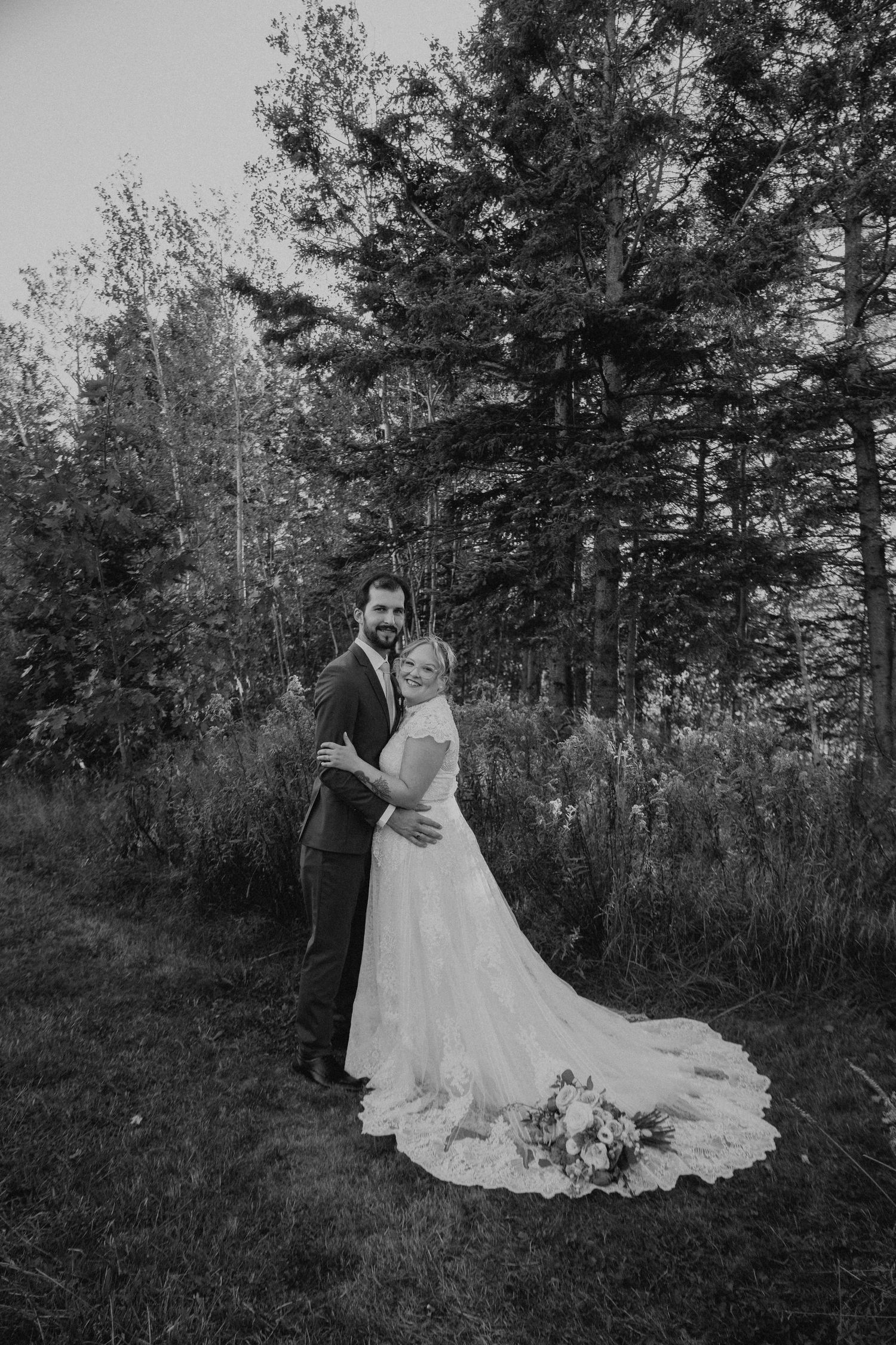 A white wedding dress with a flowing train photographed in a wooded forest setting at sunset.