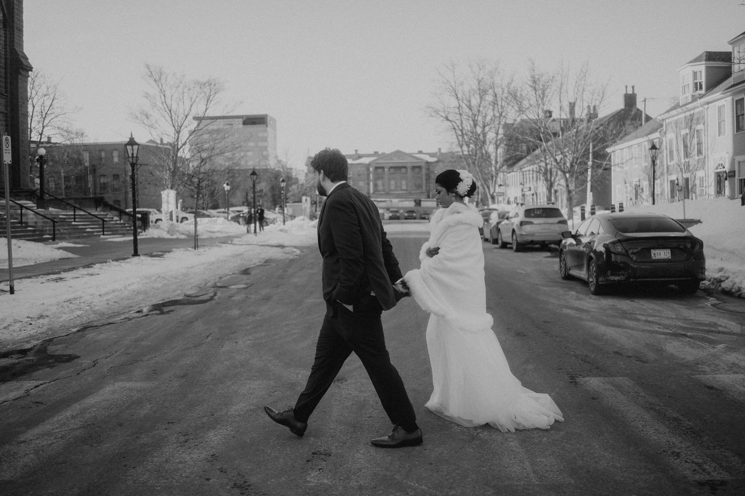 Black and white photo of newlyweds playfully running down a winter street.