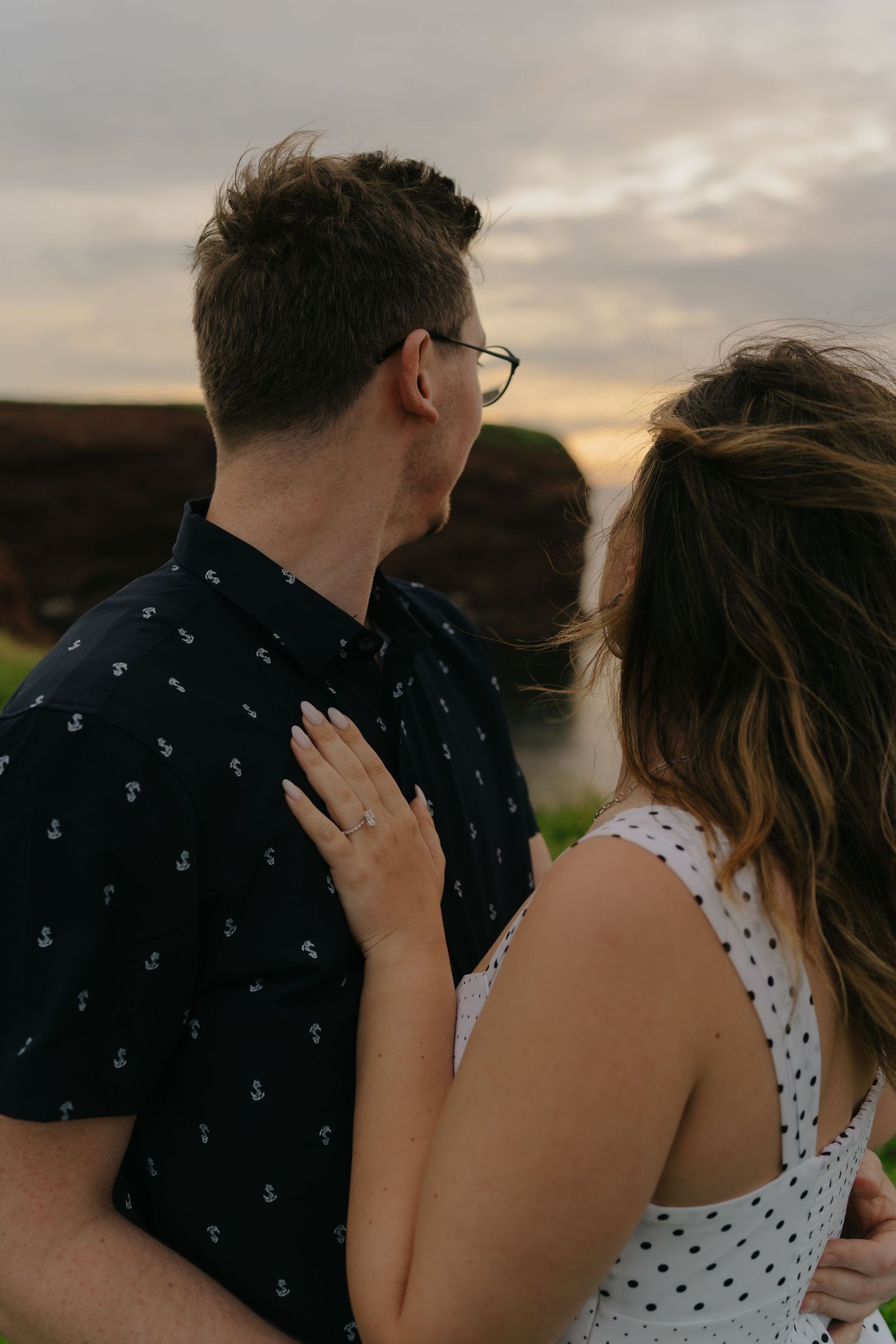 Couple sharing an intimate moment on coastal cliffs during sunset.