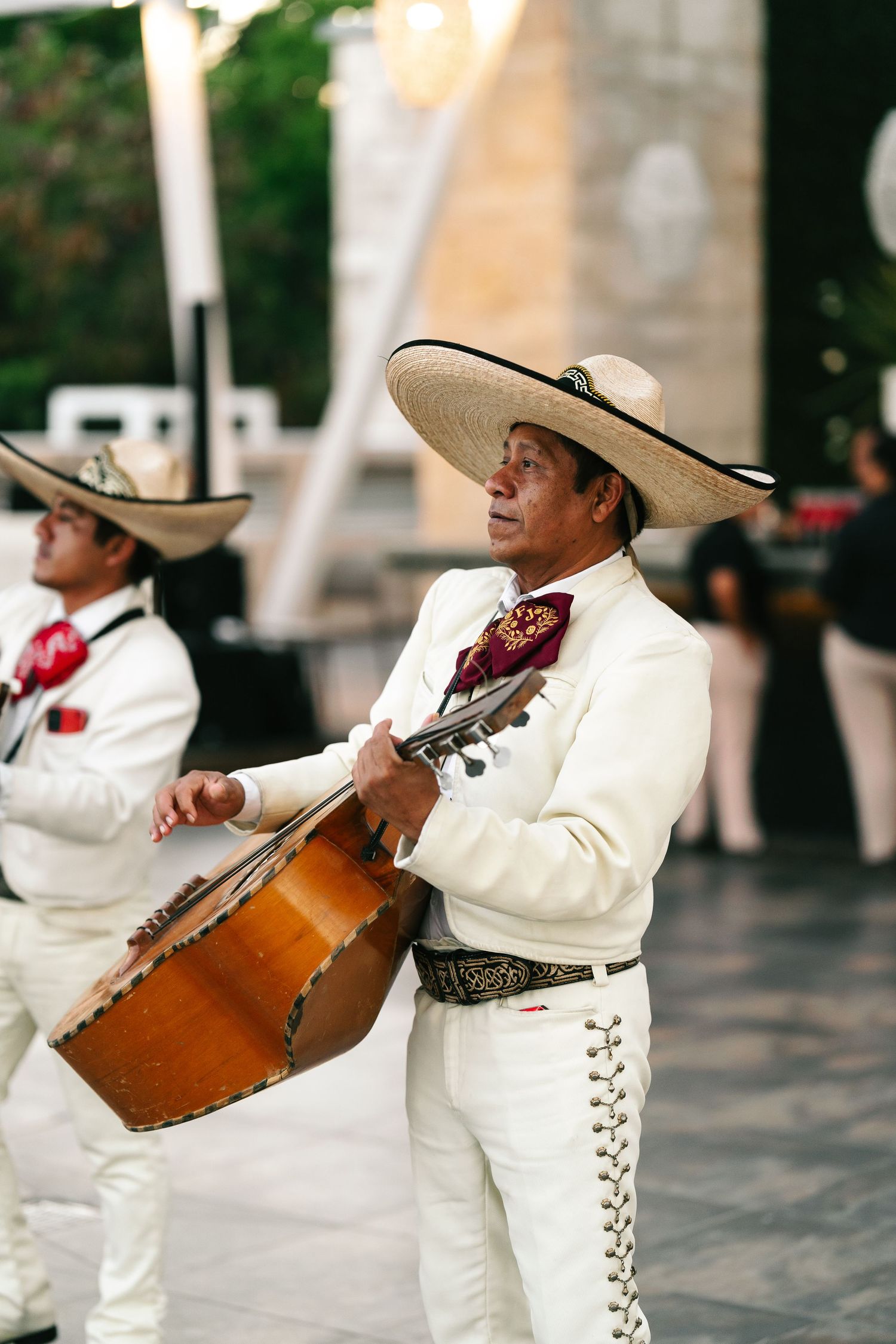 Mariachi musician in white suit and sombrero playing guitar at outdoor wedding.