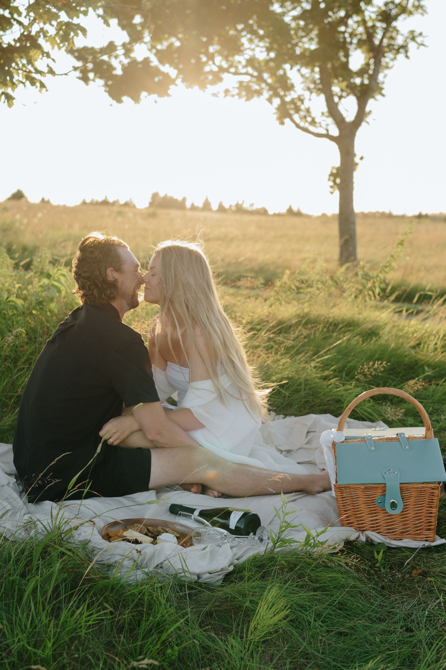 Romantic picnic scene with blanket and basket in a grassy field at golden hour.
