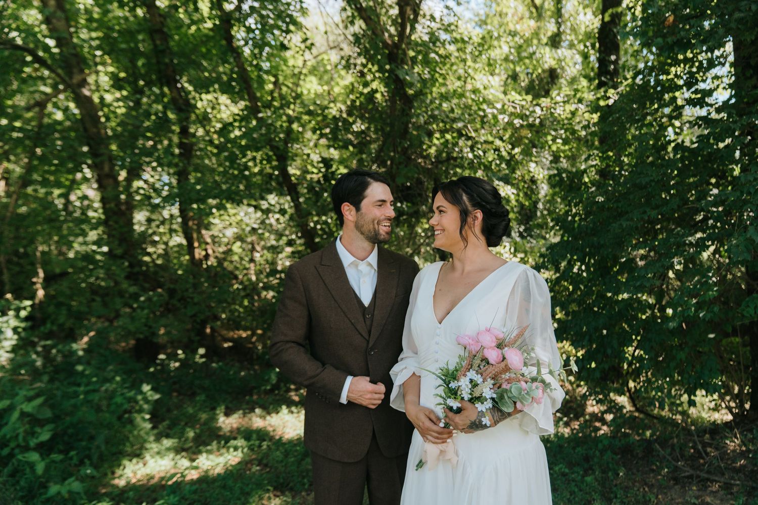 Candid wedding portrait in sunlit garden with spring greenery.