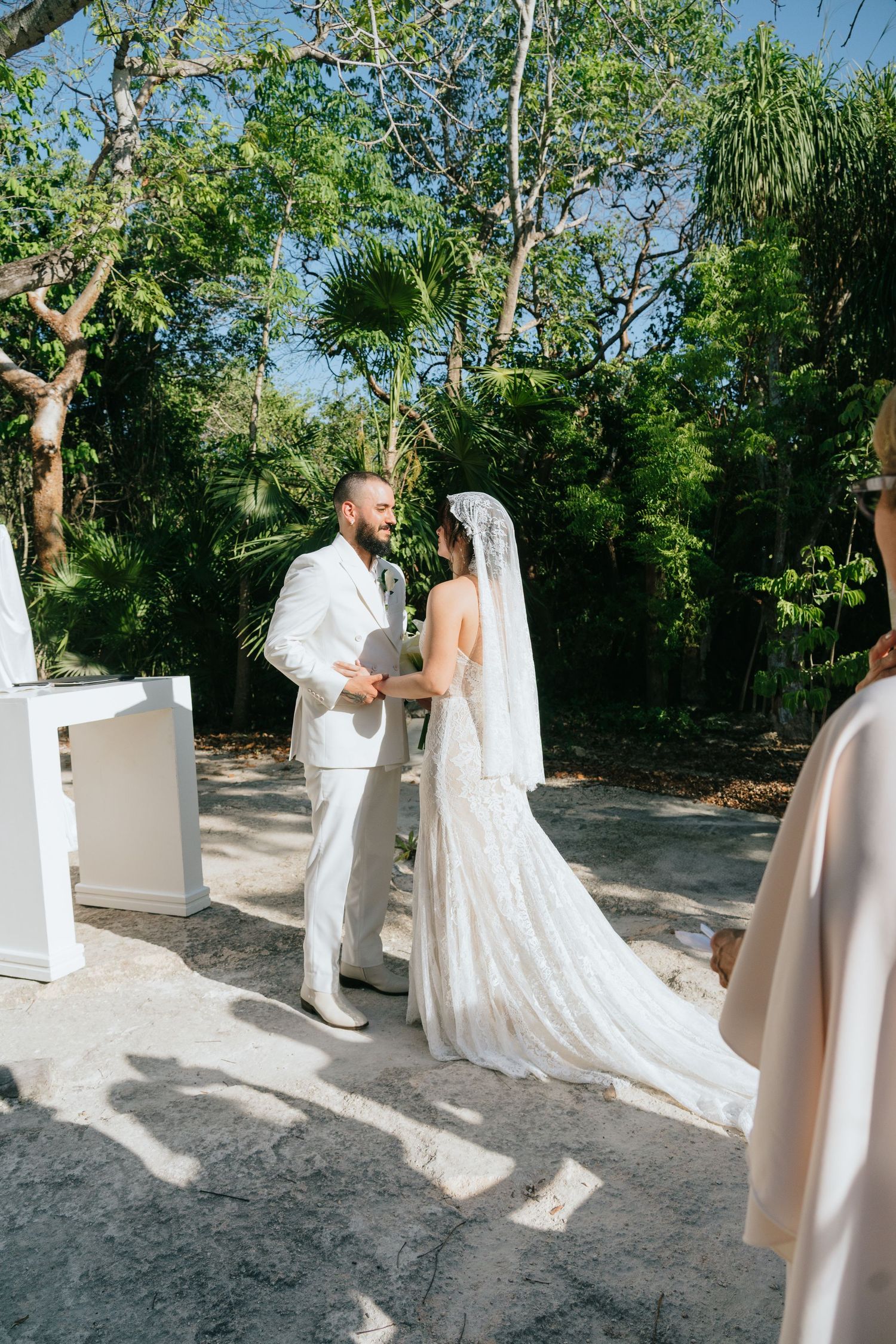 Bride and groom exchange vows outdoors surrounded by lush tropical greenery.