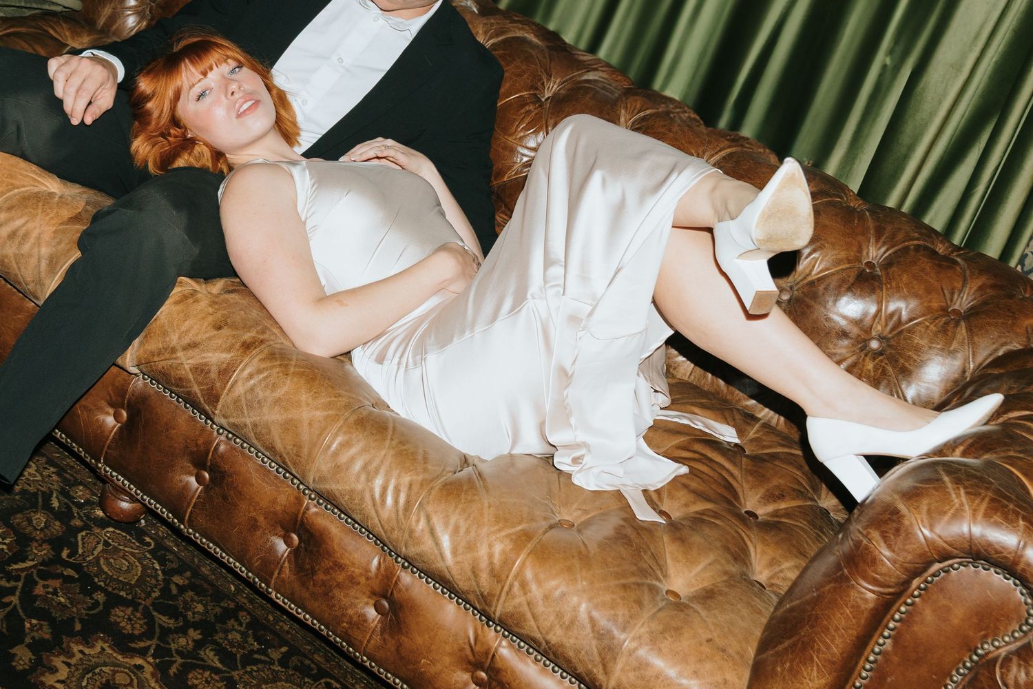 A person in white dress and boots reclines on a brown leather couch.
