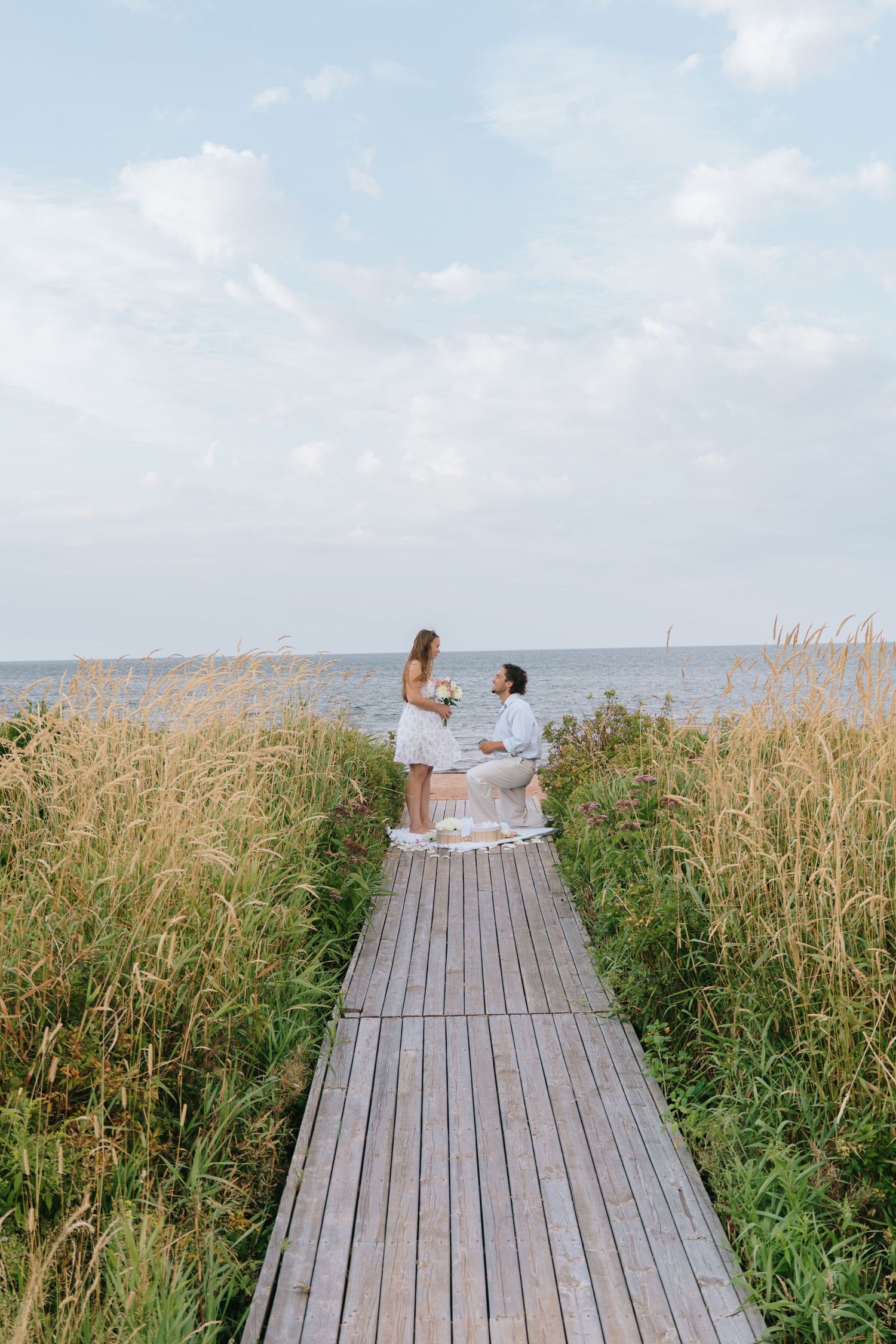 Wooden boardwalk through tall grass leading to ocean view.