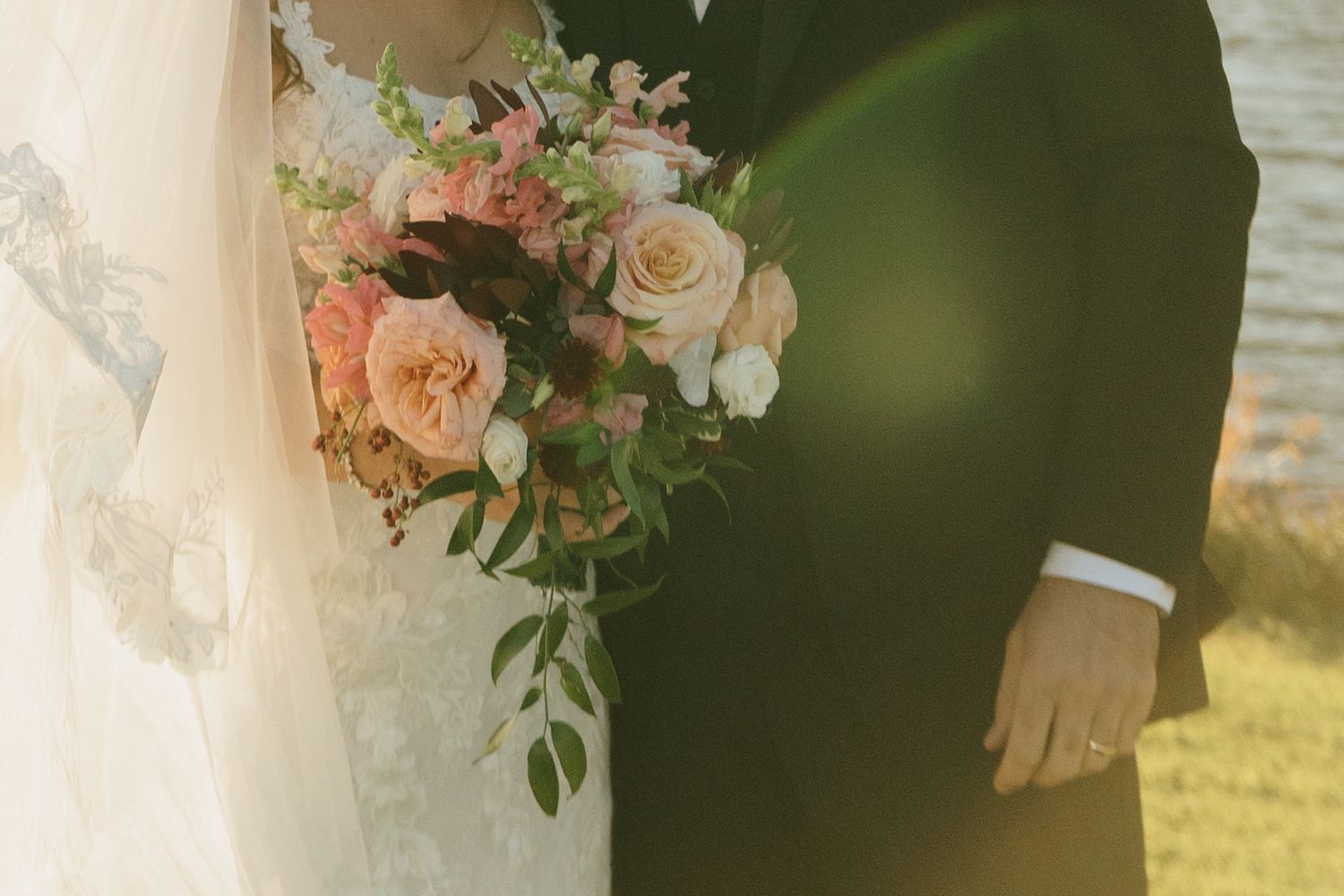Bride and groom holding a beautiful pink and white wedding bouquet with roses and greenery on their wedding day.