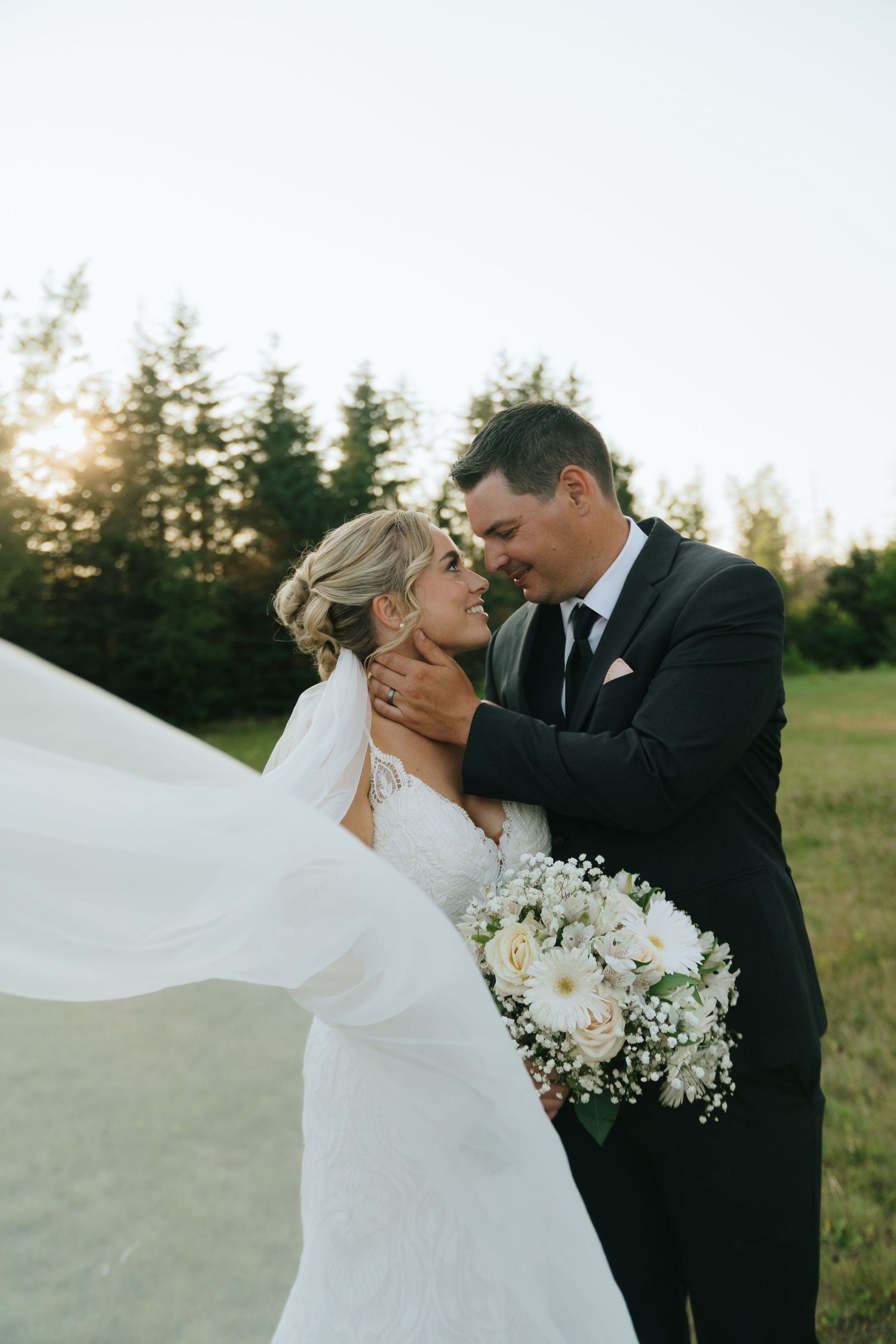 Romantic wedding portrait with bride's veil flowing in the wind against sunset light.