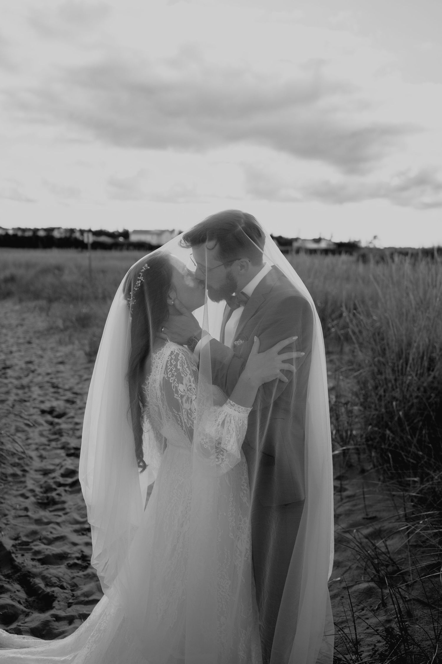Artistic black and white photograph of a wedding dress flowing in the breeze by the water.