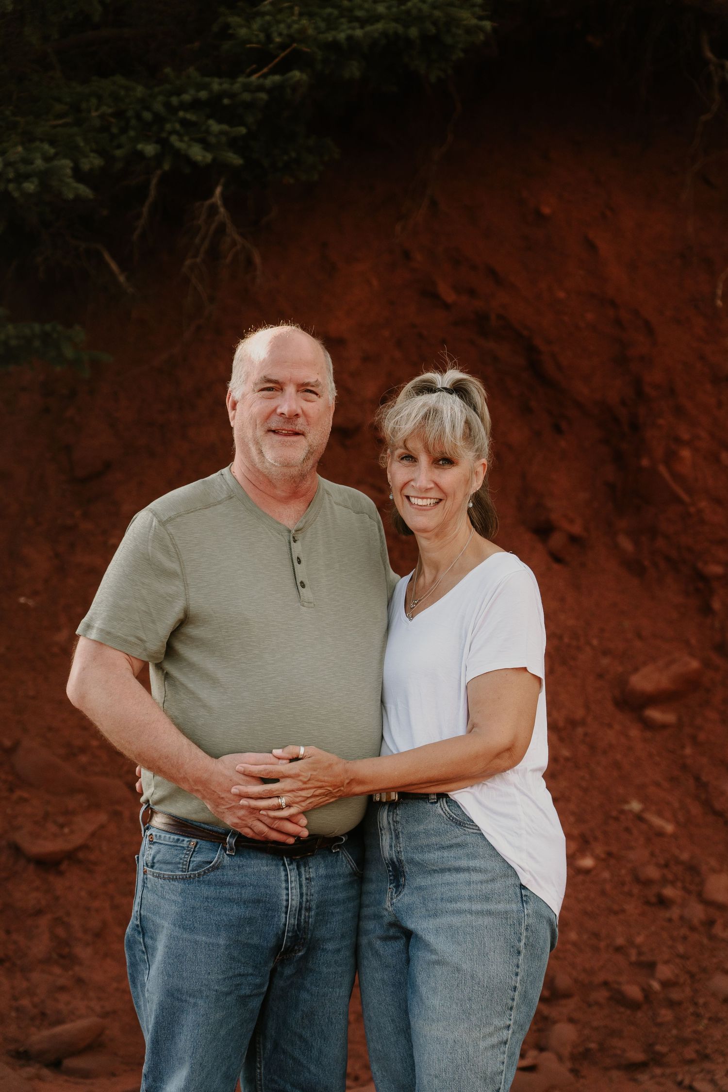 Couple posing against a dramatic red rock wall backdrop at sunset.