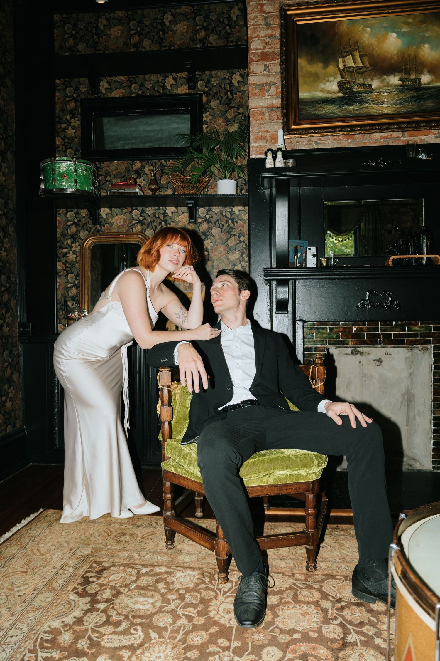 A couple in formal attire shares an intimate moment on a vintage chair in an ornate room.