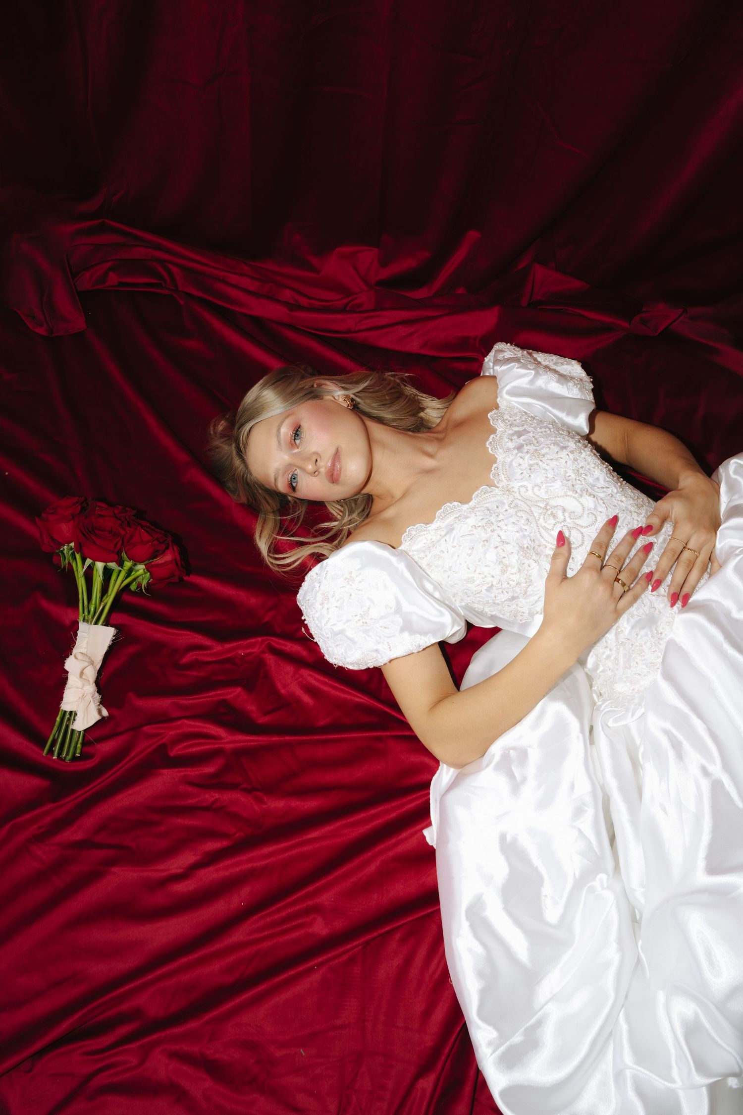 Dramatic bridal portrait on red velvet with white dress and floral bouquet.