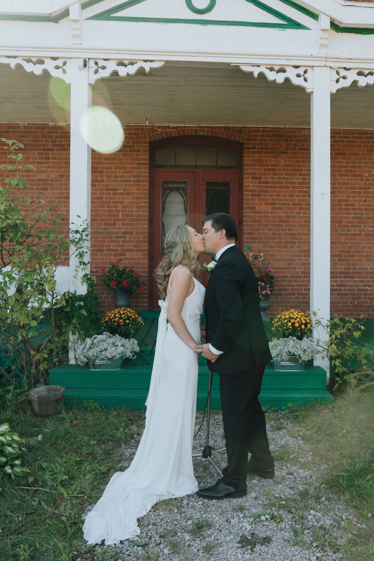A couple shares a moment on a porch of a brick building with white columns and green accents.