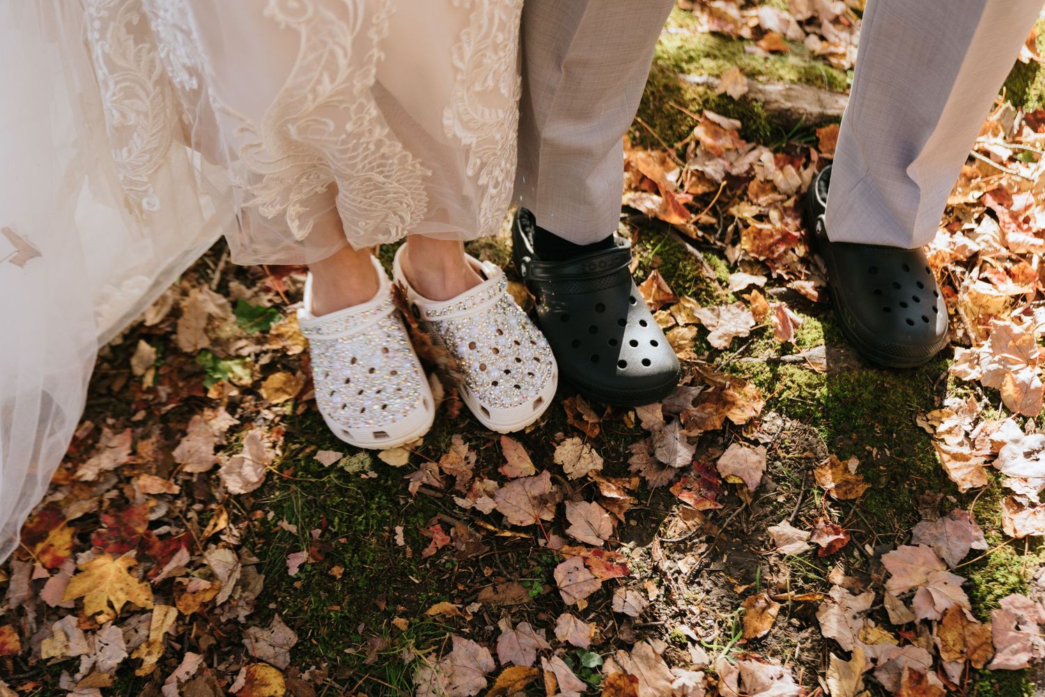 Wedding couple's feet standing on autumn leaves, showing white bridal shoes and dark formal shoes.