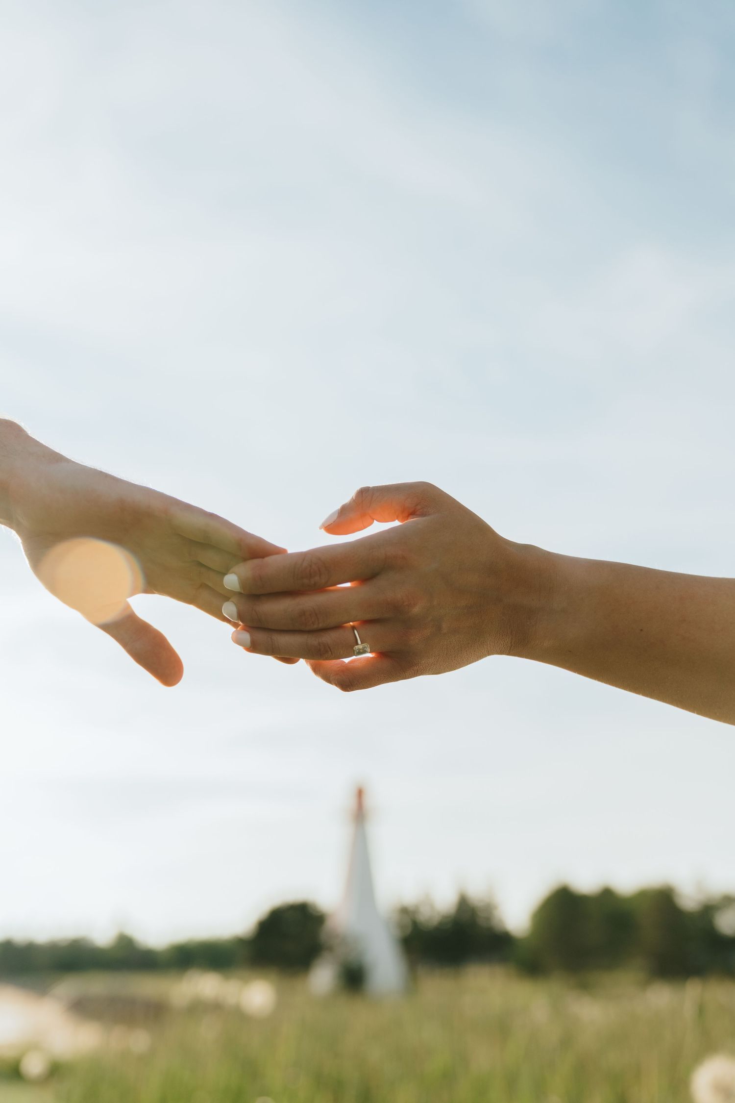 Close-up of hands with wedding ring against sunlit sky and church spire.