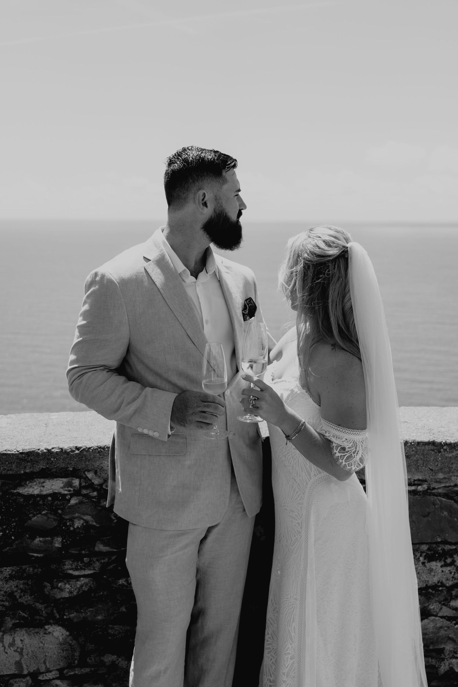 A romantic black and white wedding photo series showing a couple sharing champagne by the ocean.
