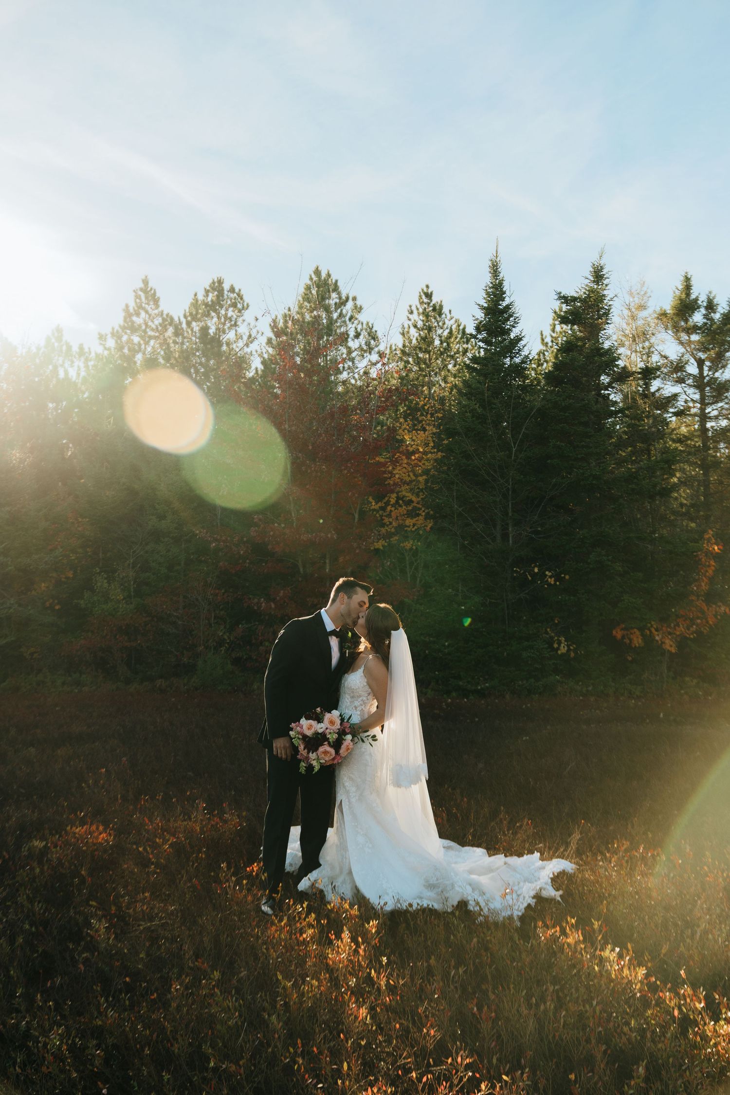 Newlyweds embrace in golden sunlight with autumn forest backdrop.