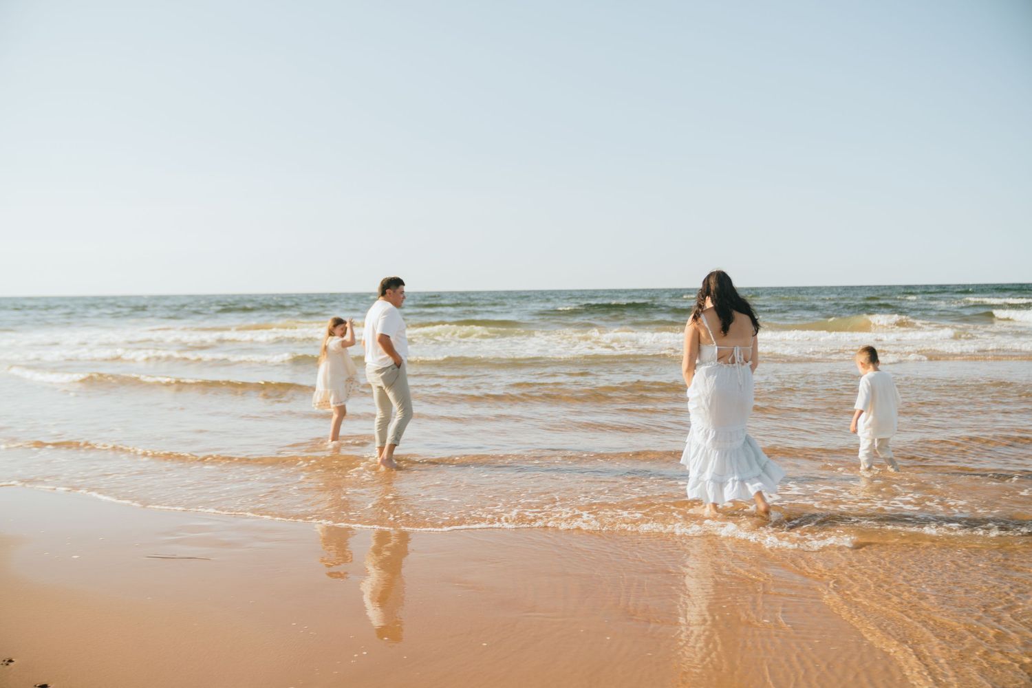 People walking and playing along a sandy beach at sunset.