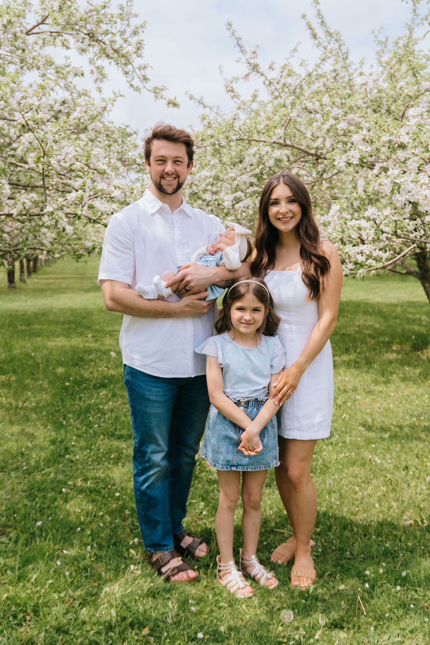 Family portrait session in a blooming apple orchard on a sunny spring day.