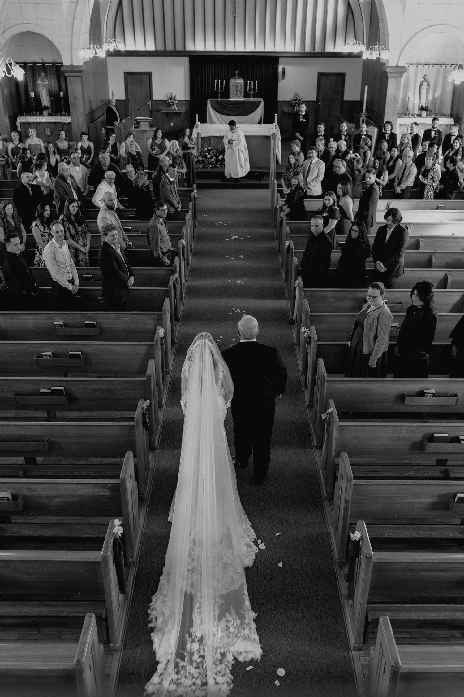 Aerial black and white photo of a bride walking down the church aisle with her father during a wedding ceremony.