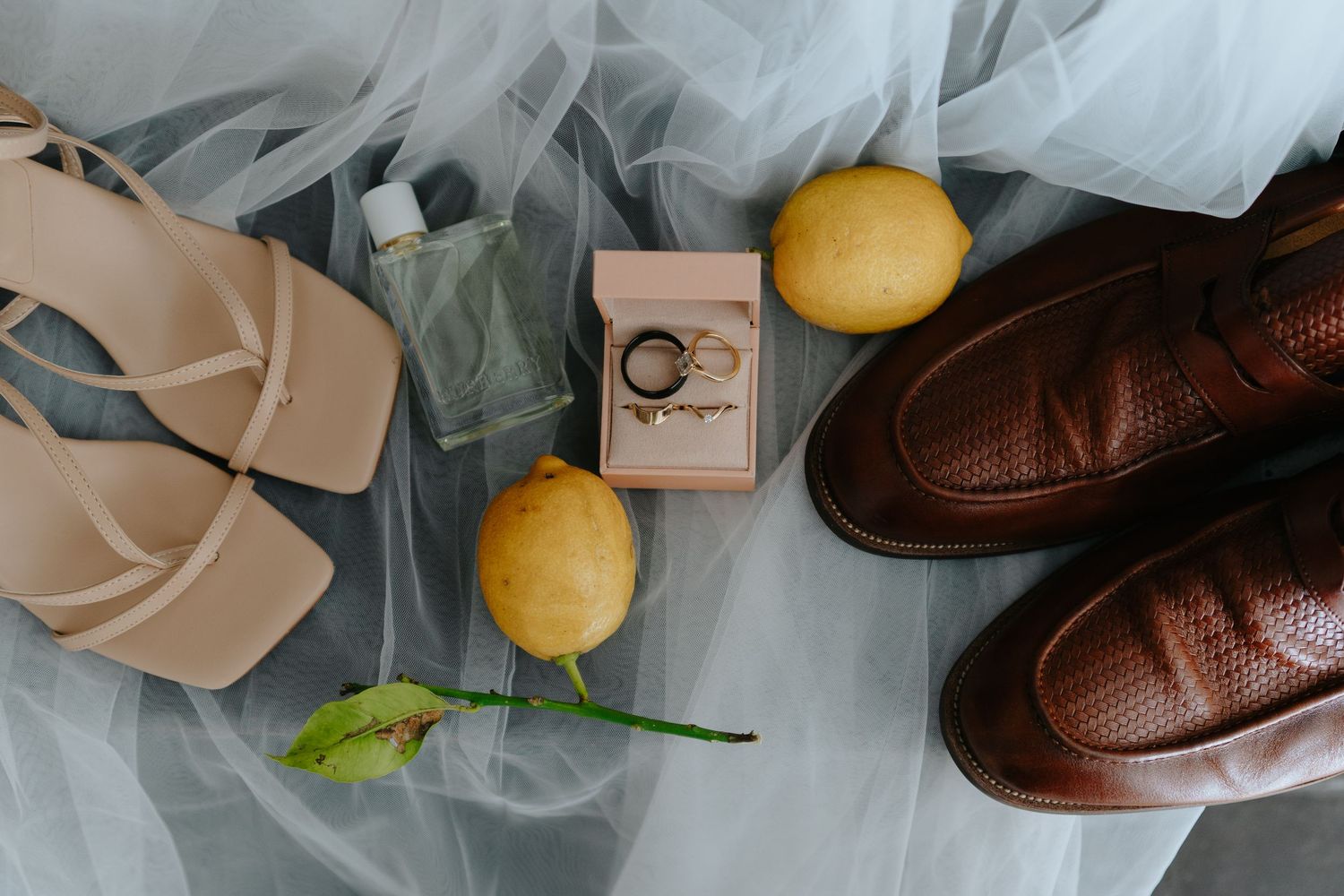 Brown leather loafers and fresh yellow lemons arranged artistically on light blue tulle fabric.