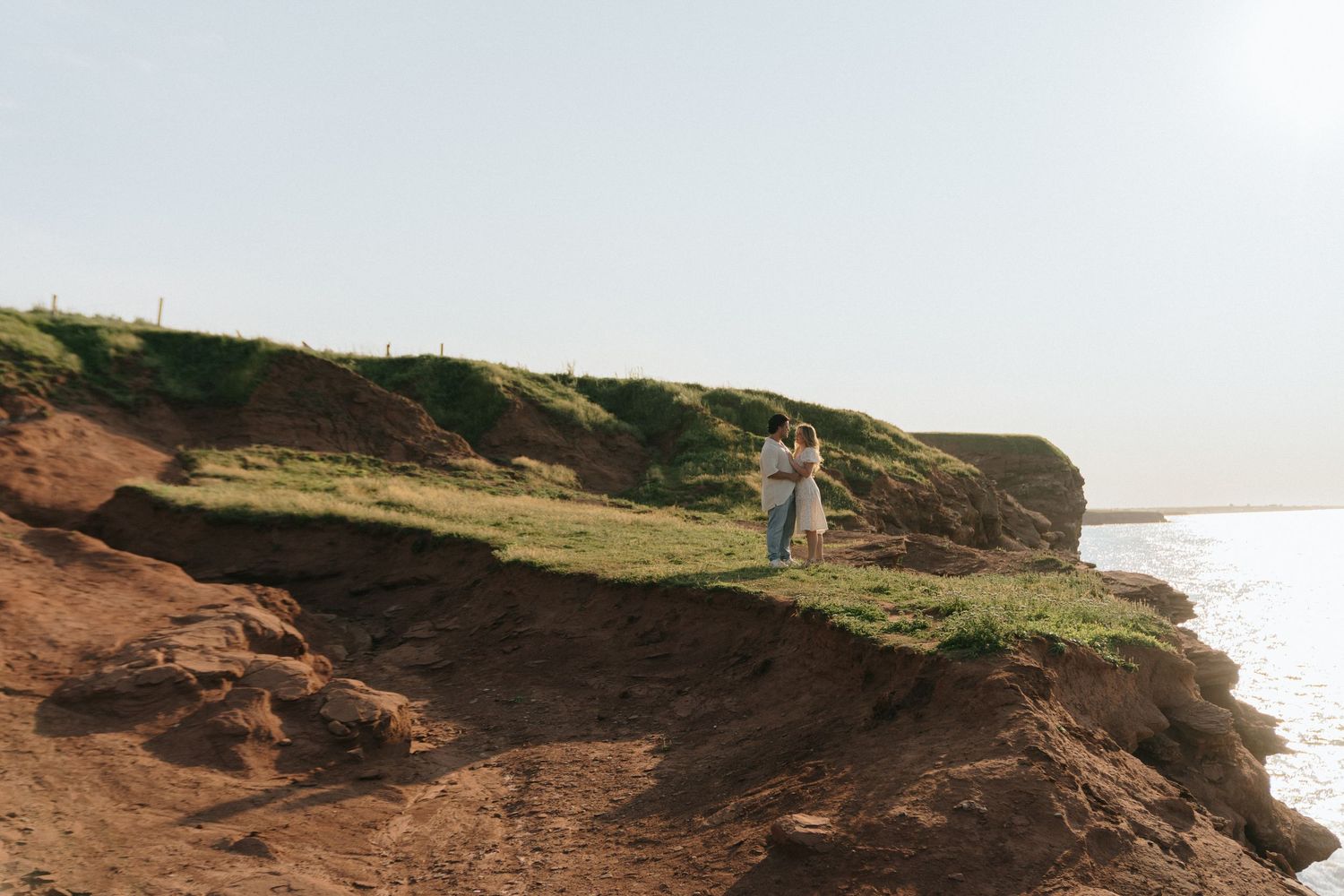 Scenic coastal cliffs with rugged red rock formations and green vegetation overlooking the ocean at sunset in Cape Tryon, PEI