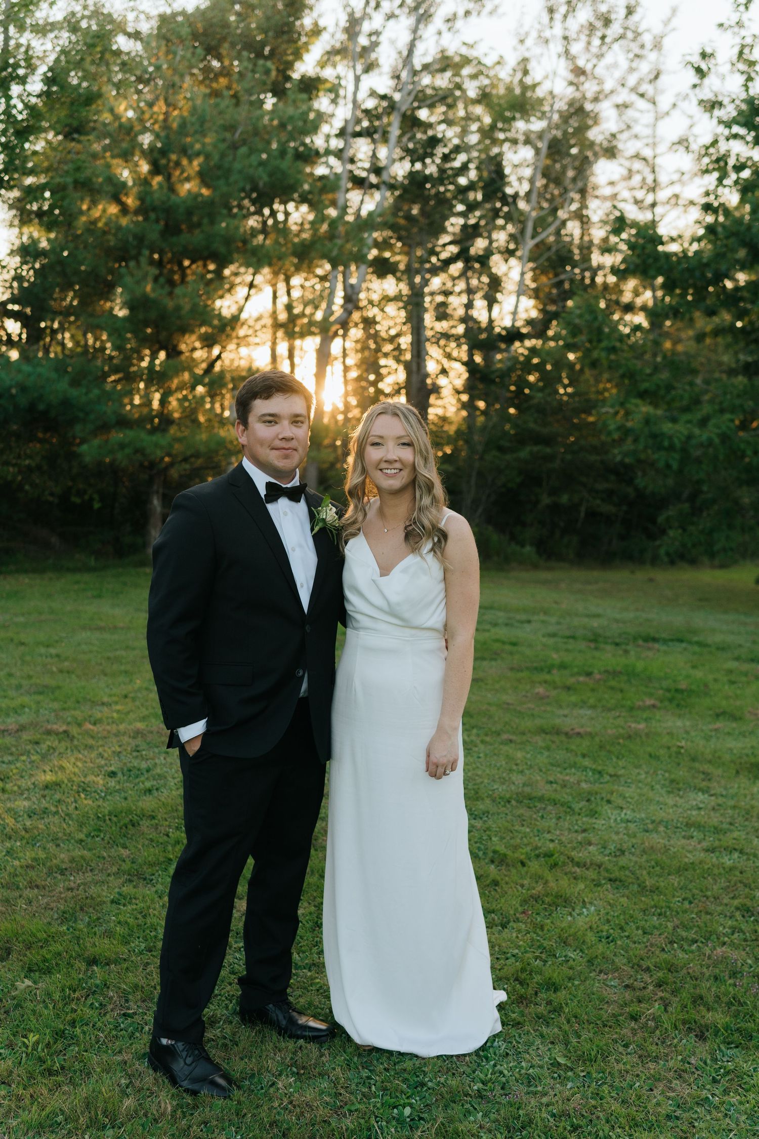 A wedding couple poses together on grass during golden hour.