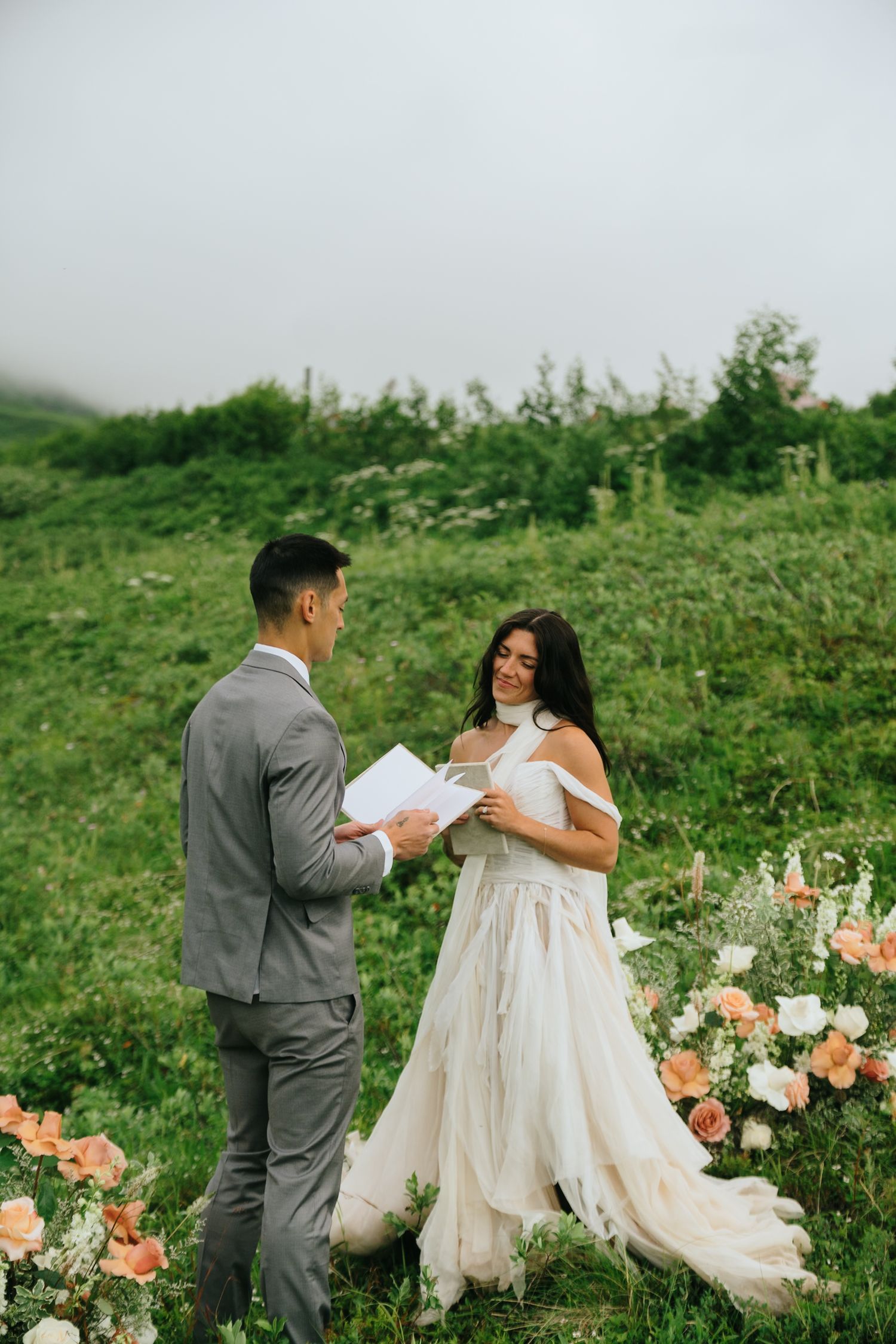 Wedding couple exchanging vows in a scenic mountain meadow with peach floral arrangements in Alaska