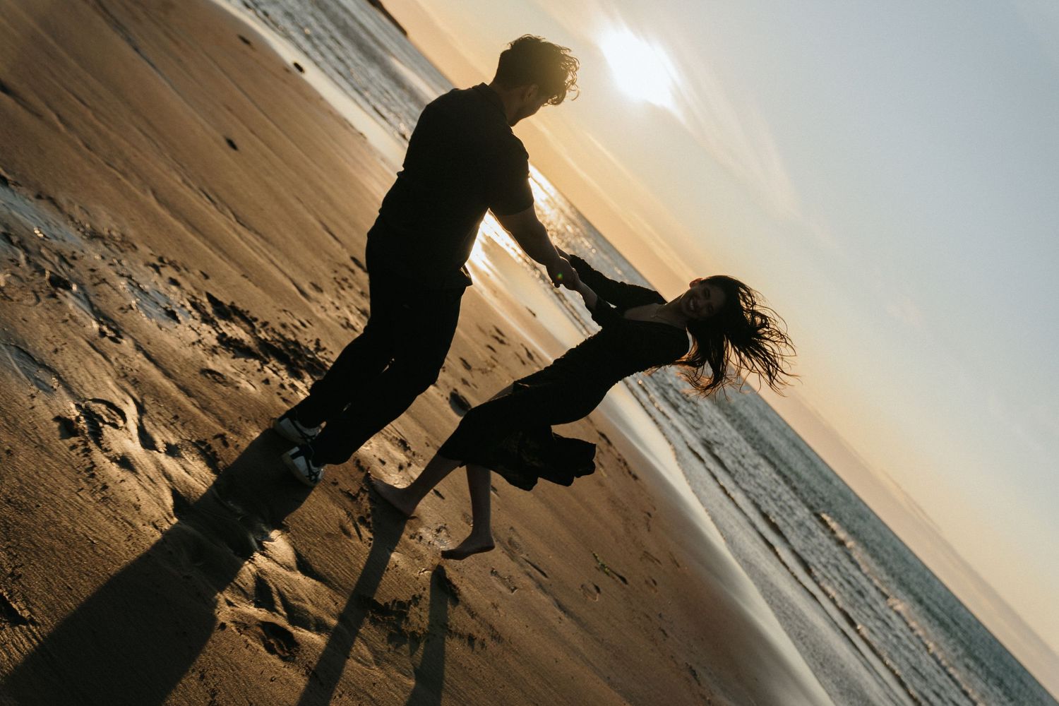 Silhouetted figures play and splash in shallow ocean water at sunset creating a joyful beach scene.