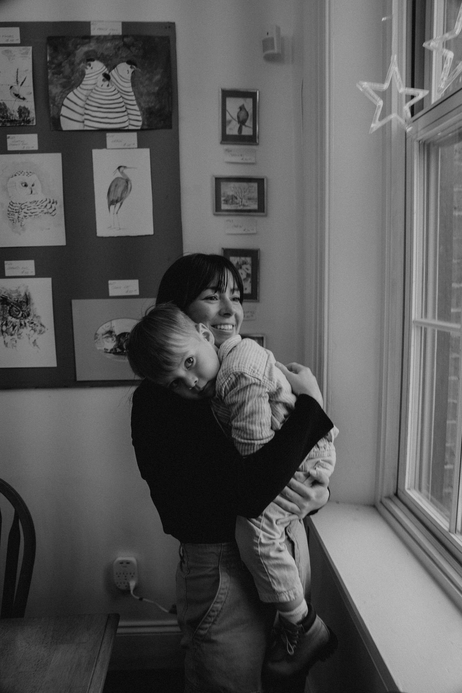 A tender moment by a window with artwork displayed on the wall in black and white.
