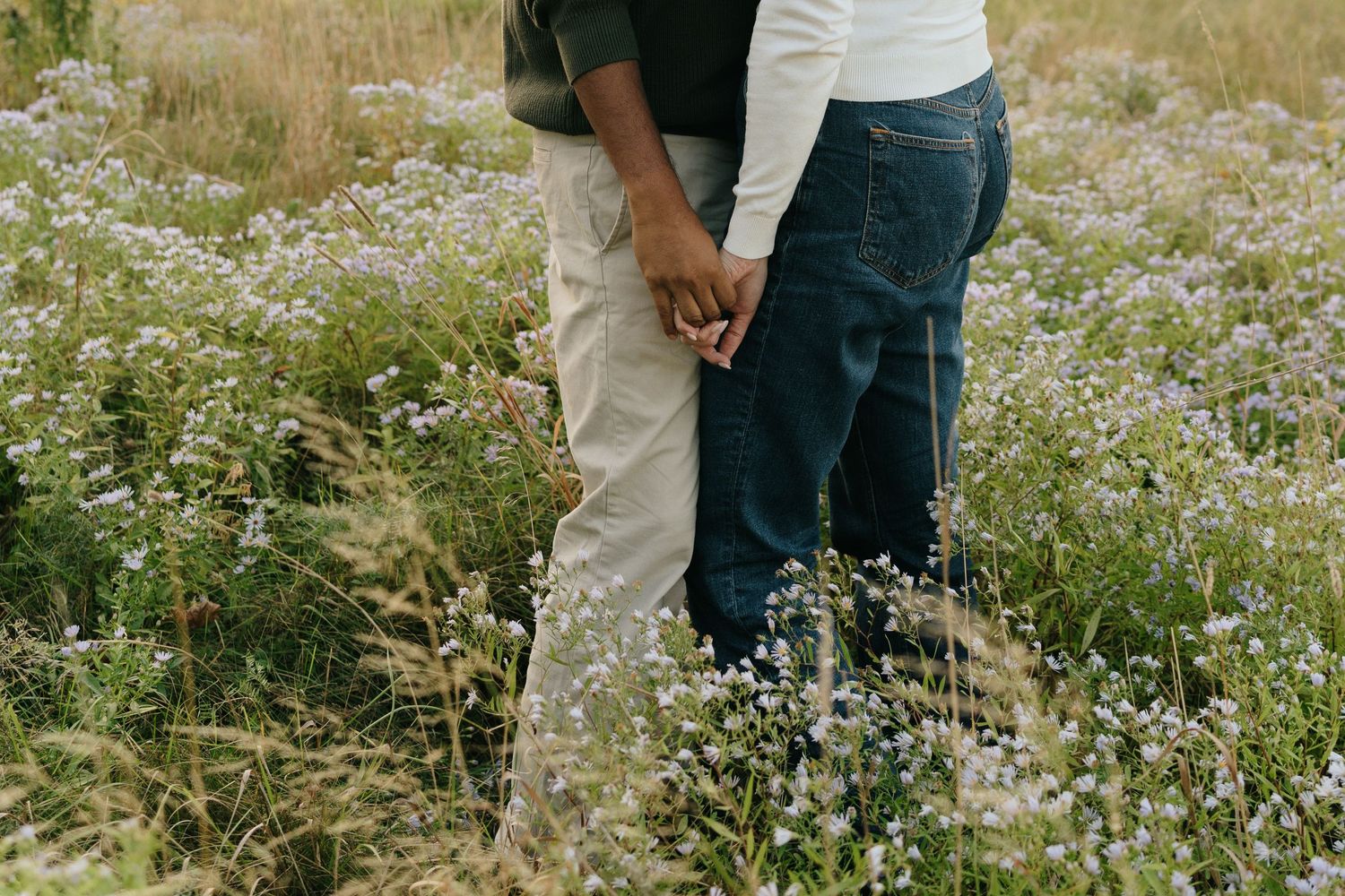 A couple holds hands while walking through a wildflower meadow.