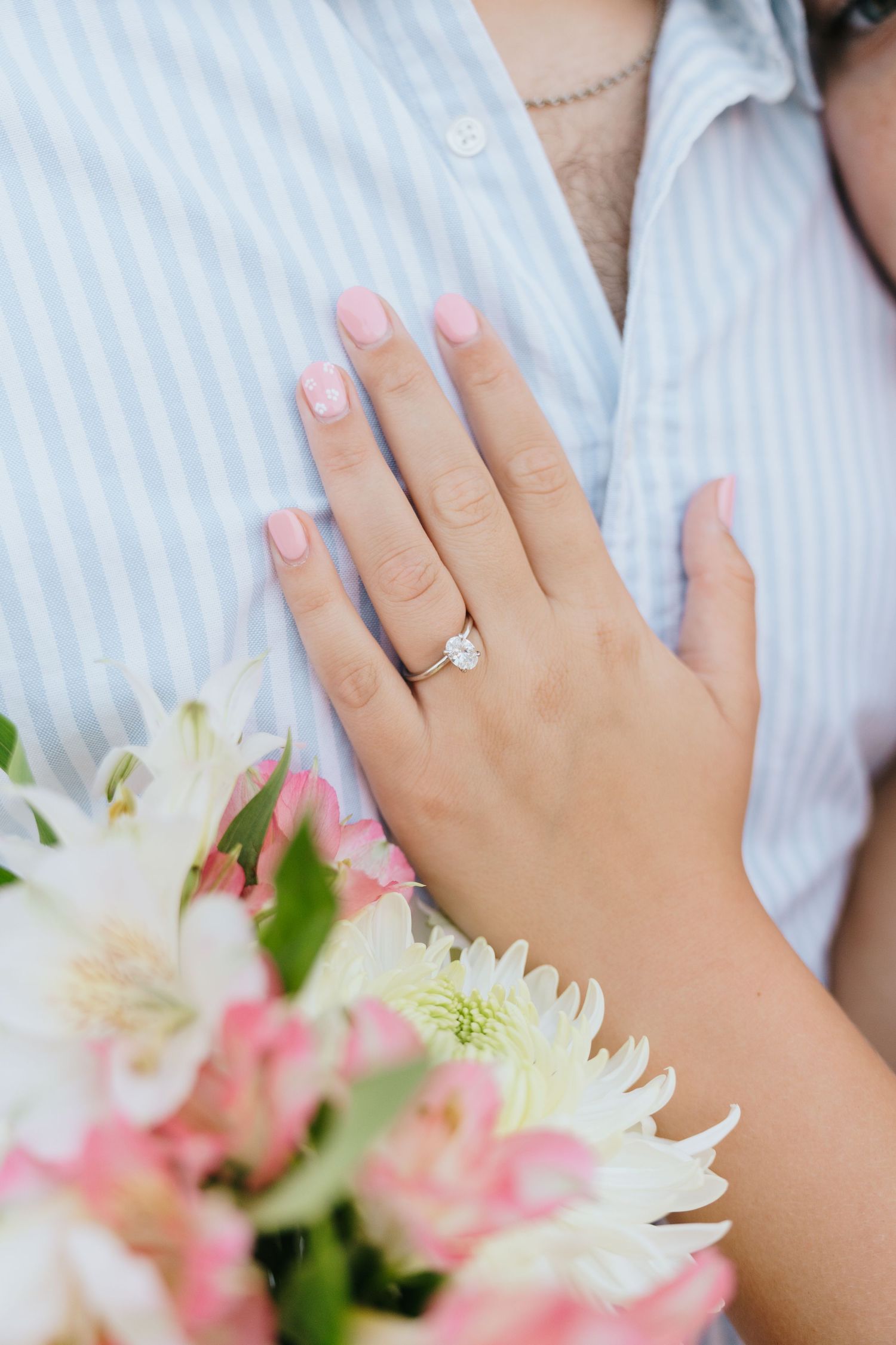 Close-up of hands with an engagement ring and white lilies in a romantic wedding detail shot.